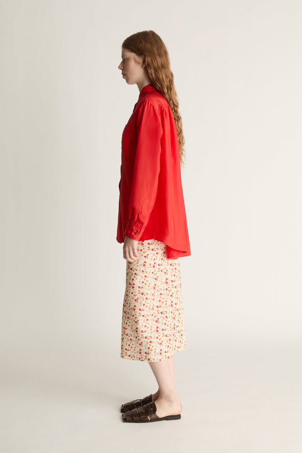 Person wearing a red shirt and patterned skirt on a plain background
