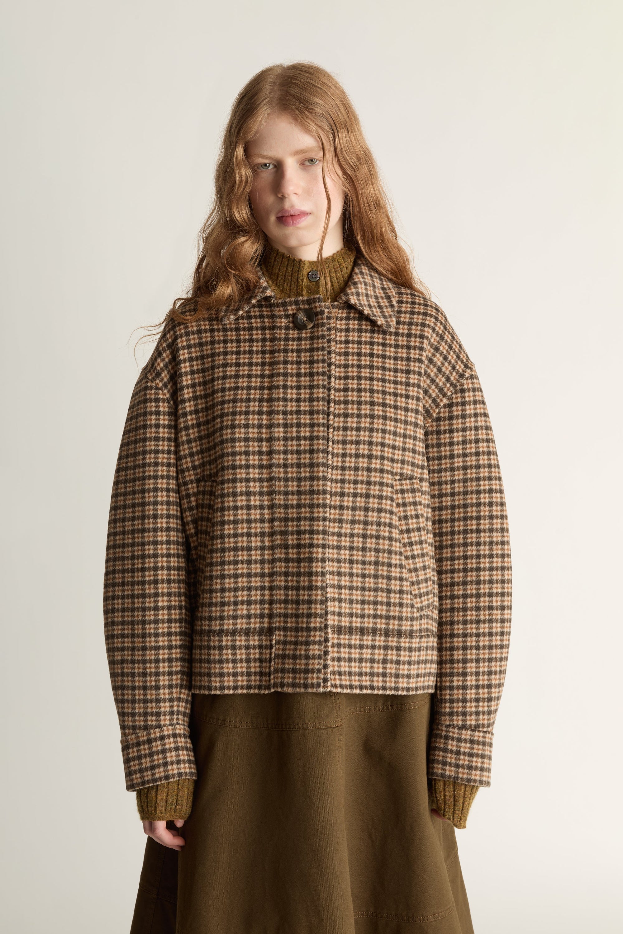 Woman wearing a plaid jacket and brown skirt on a white background
