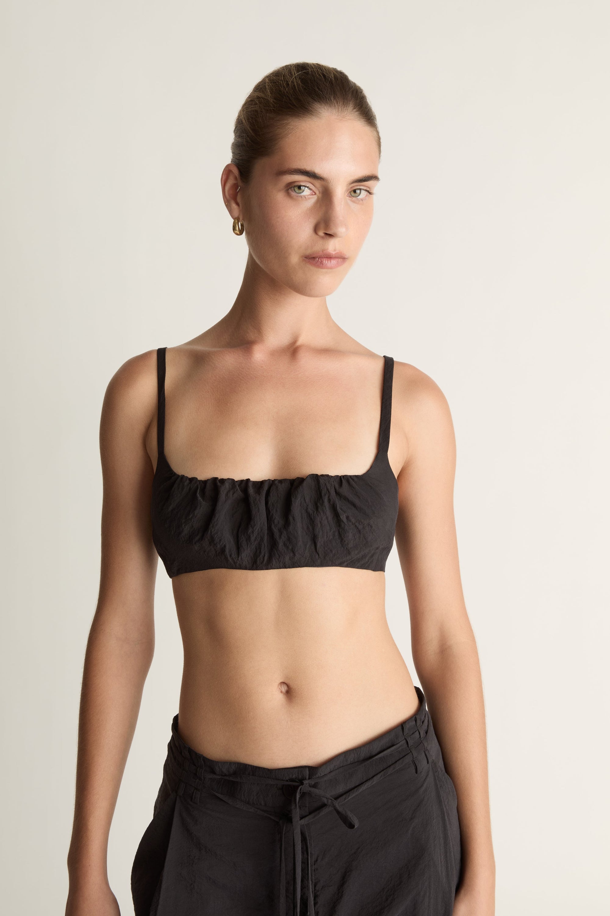 Woman wearing a cropped black top and wide-leg pants on a plain background