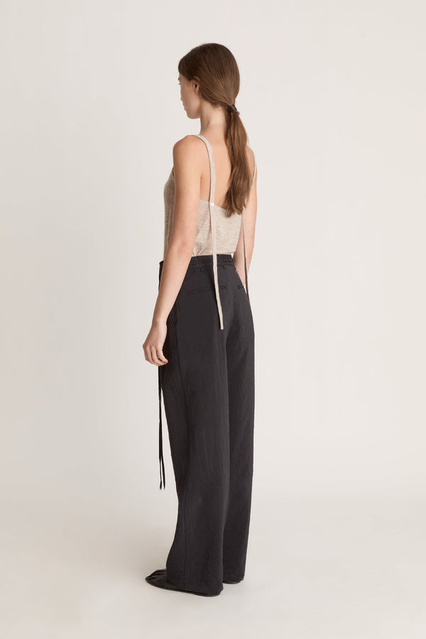 Woman wearing a beige tank top and black pants on a white background