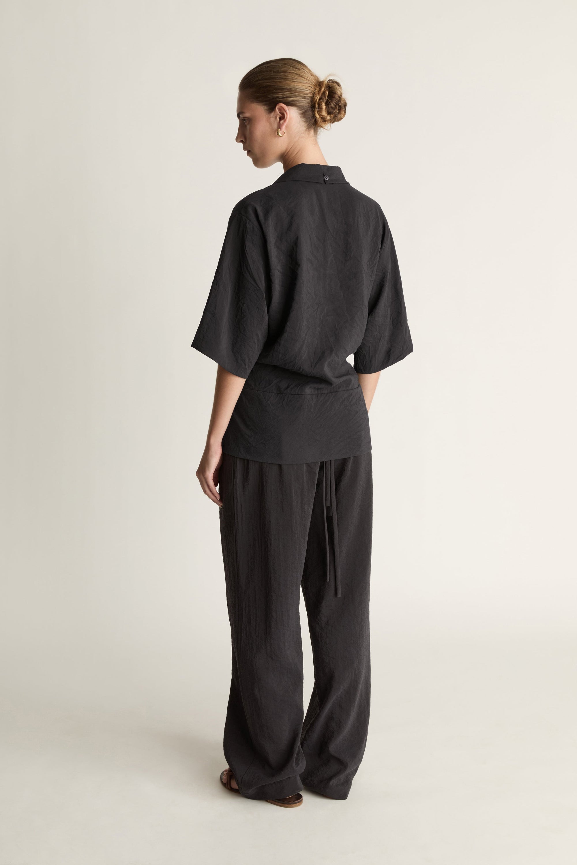 Person wearing a black wrap top with black trousers on a plain background