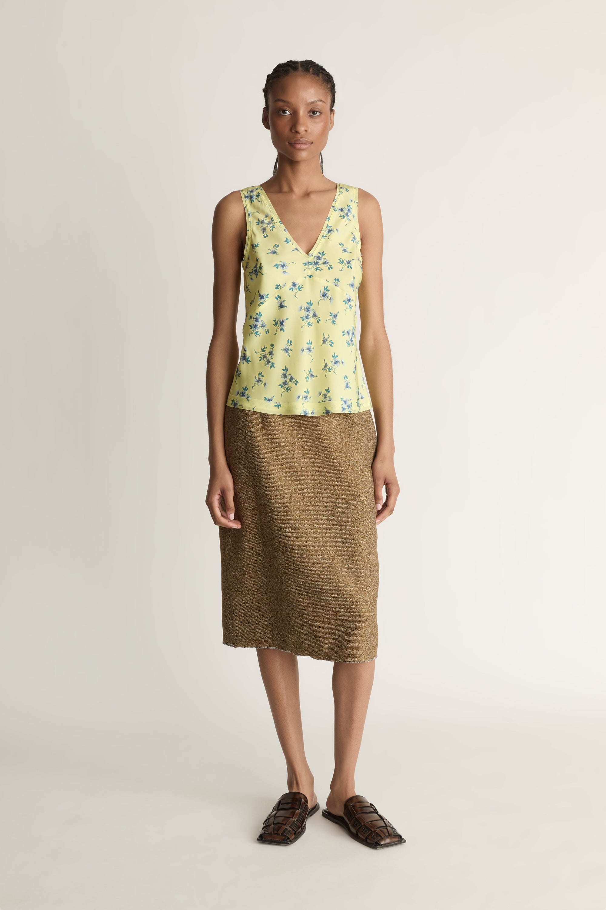 Woman wearing a yellow floral sleeveless top and brown skirt on a white background