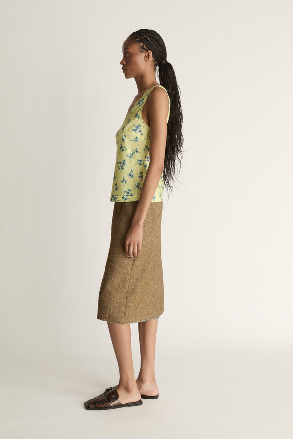 Woman wearing a yellow floral sleeveless top and brown skirt on a white background