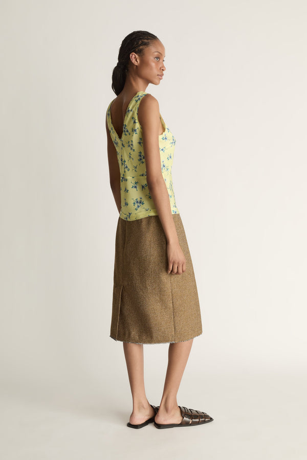 Woman wearing a yellow floral sleeveless top and brown skirt on a white background
