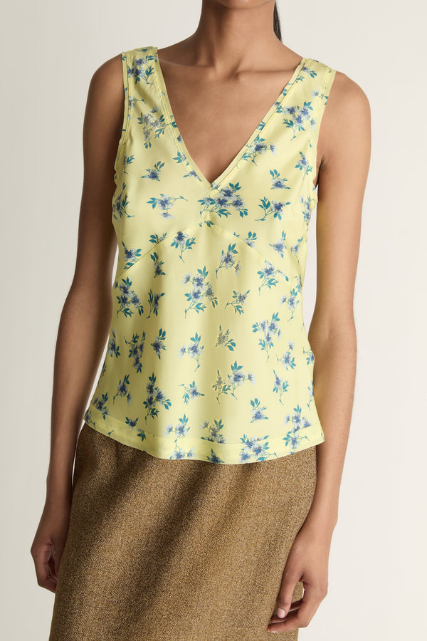 Woman wearing a yellow floral sleeveless top and brown skirt on a white background