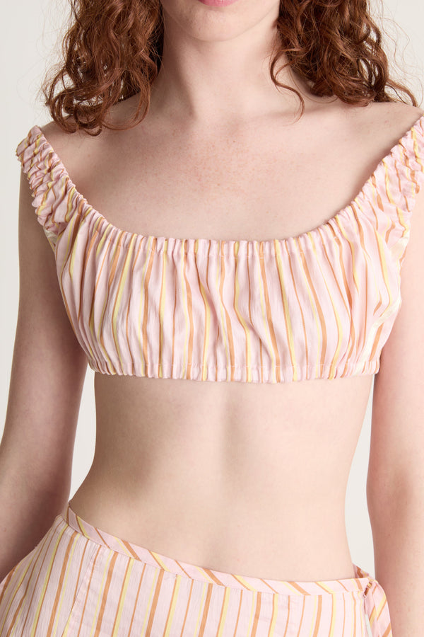 Woman wearing a pink striped crop top and skirt on a plain background