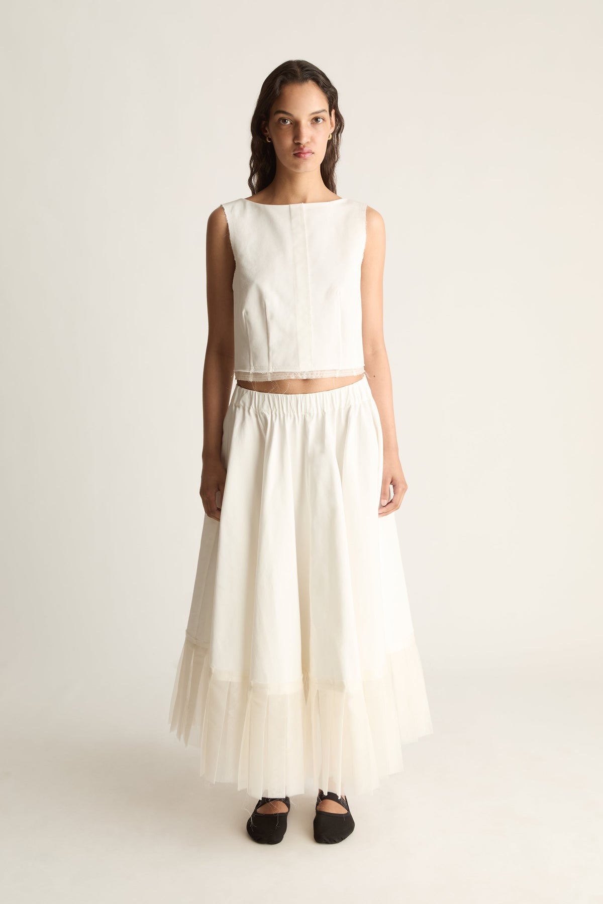 Front view of a full cream maxi skirt with an elasticated waist and a sheer layered hem, worn with a cropped top.
