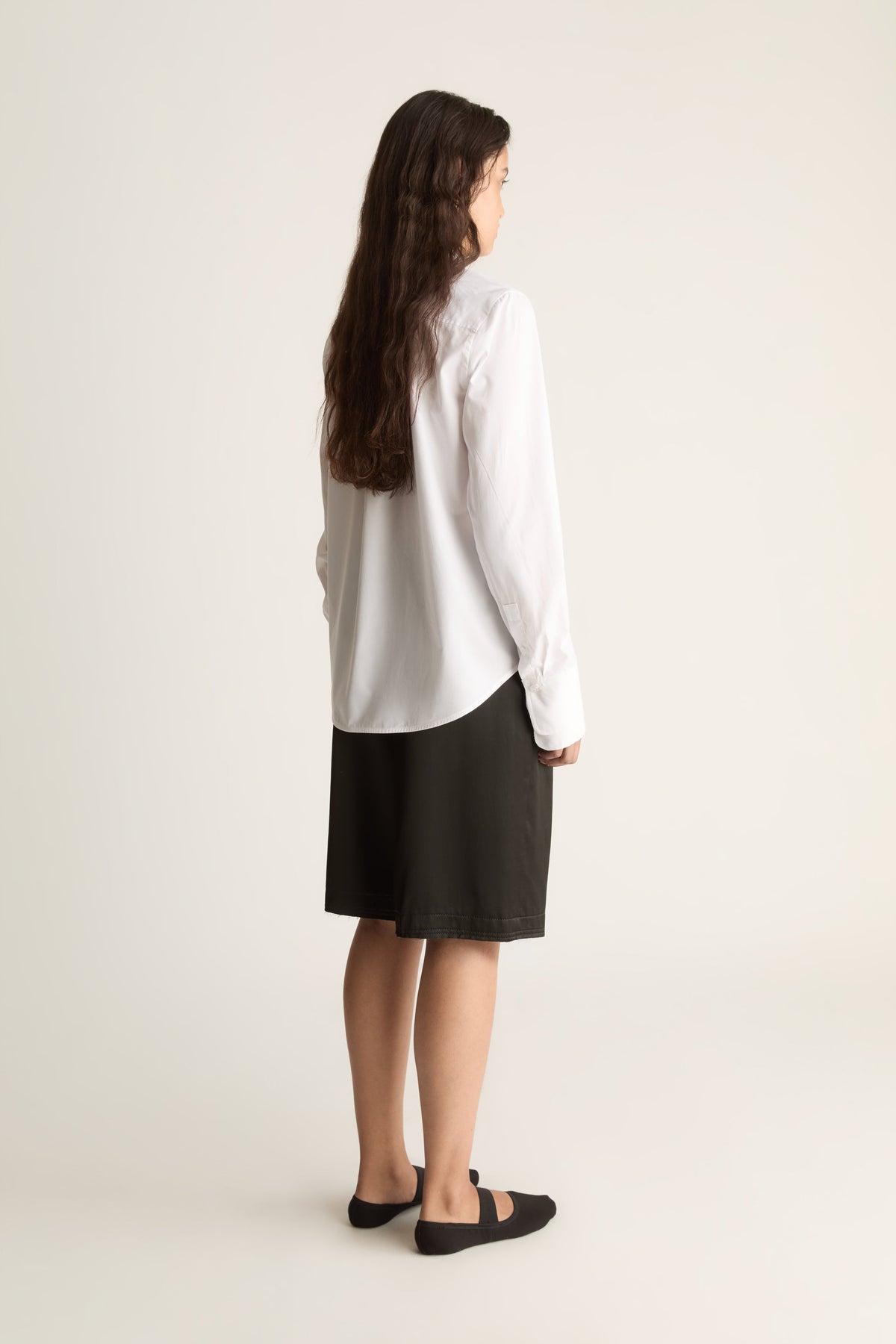 Back view of a woman with long wavy hair in a white shirt with curved hem and black knee-length shorts