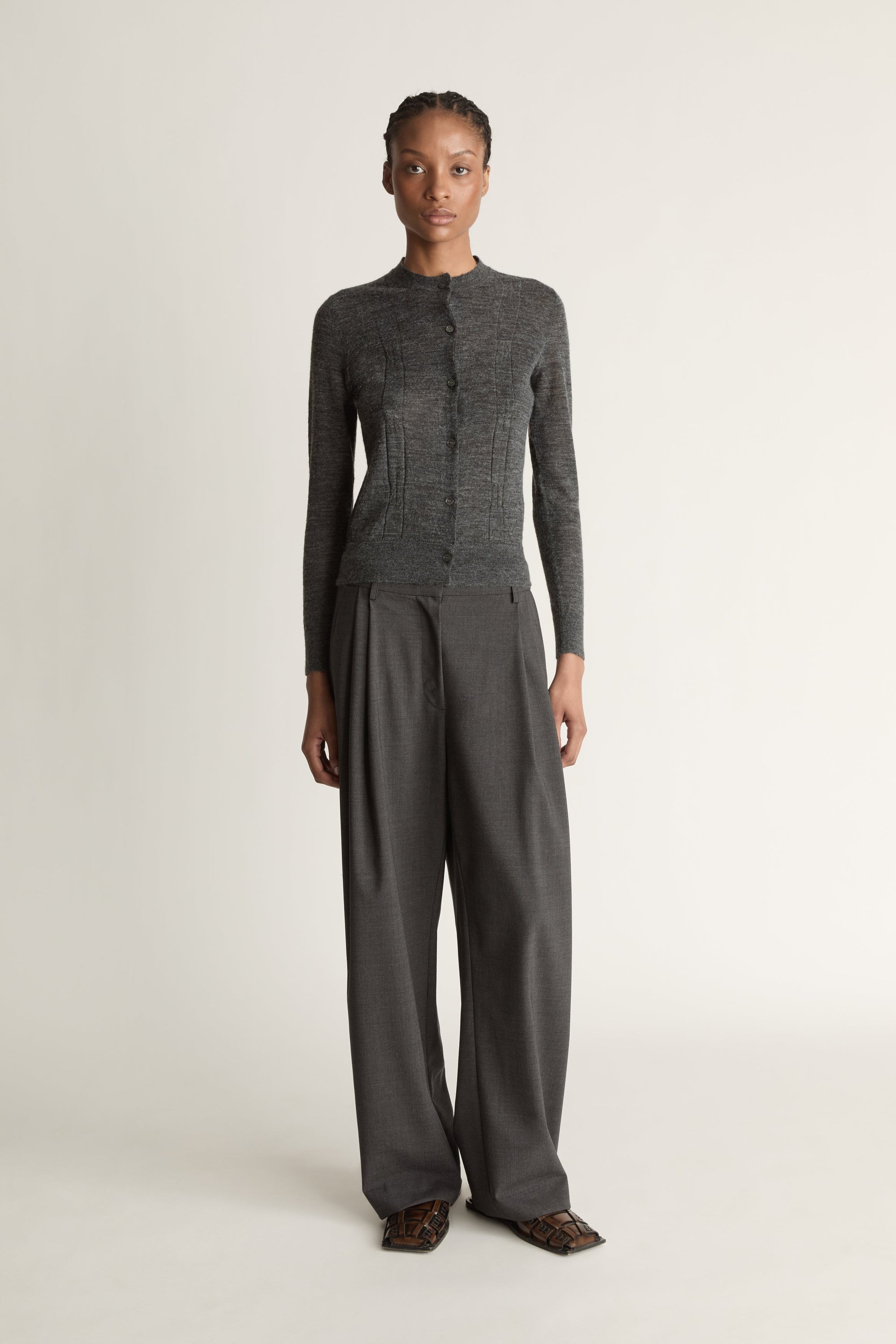 Woman wearing a grey cardigan and grey trousers on a white background