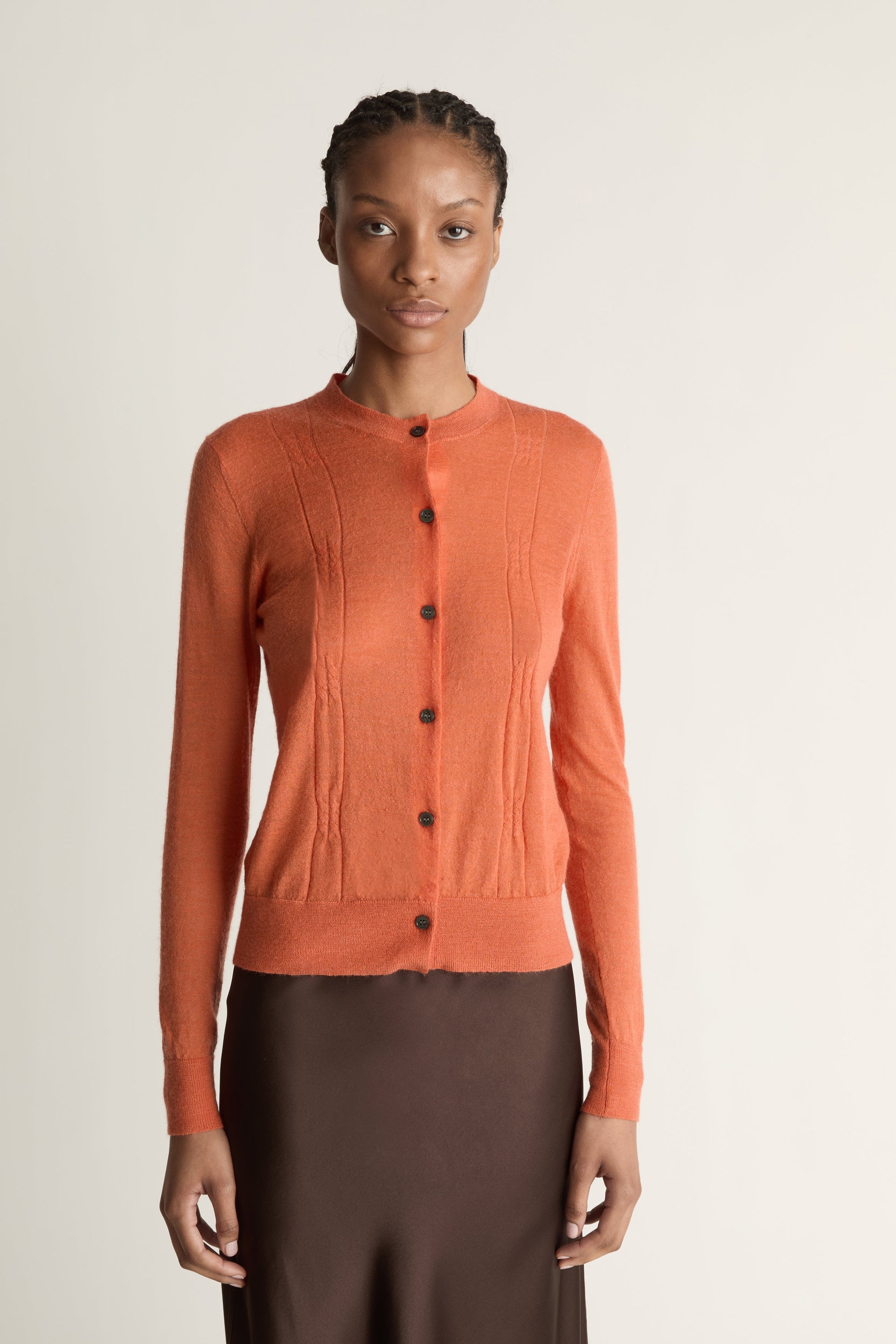 Woman wearing an orange cardigan and brown skirt on a white background
