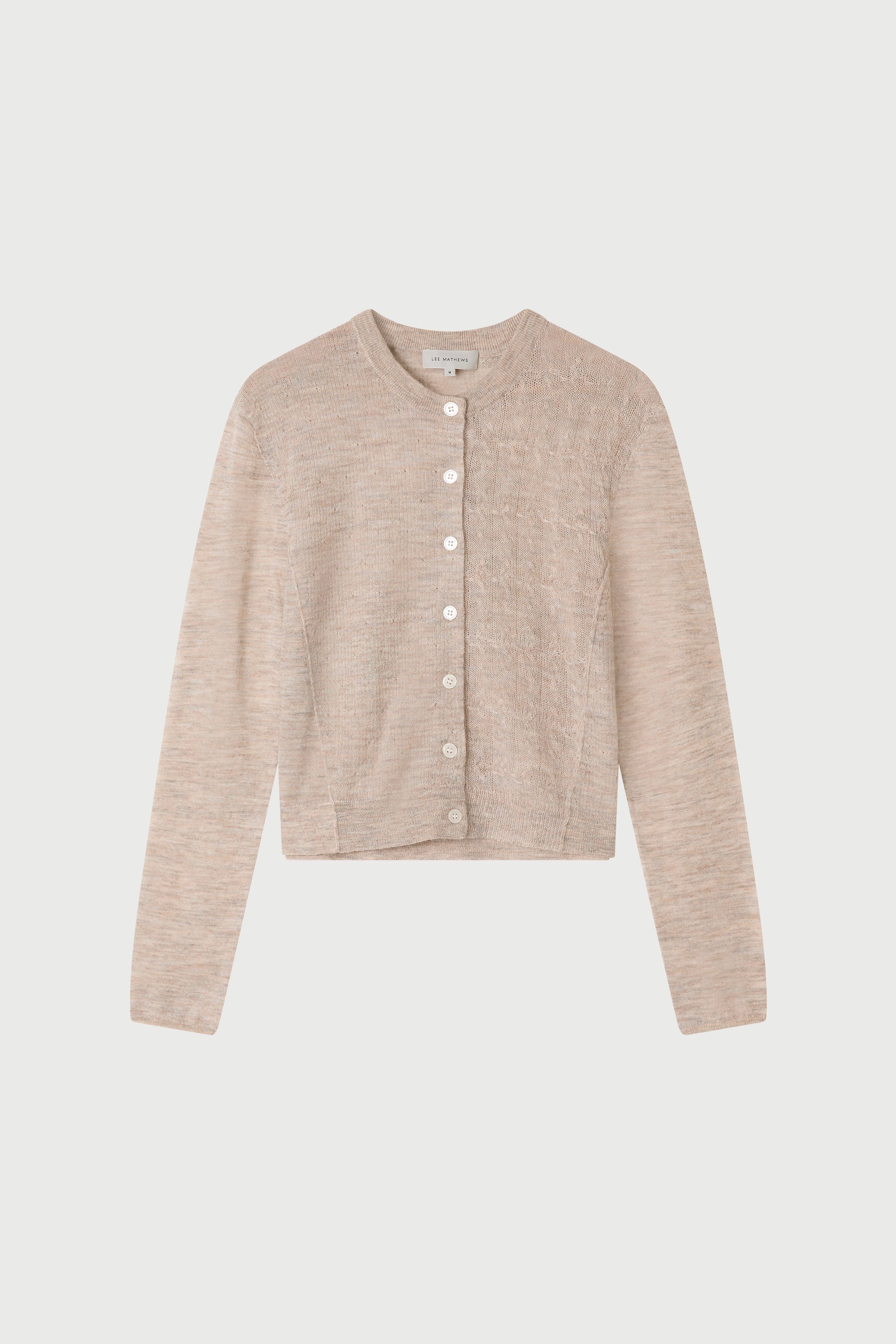 Person wearing a beige cardigan and dark jeans on a white background