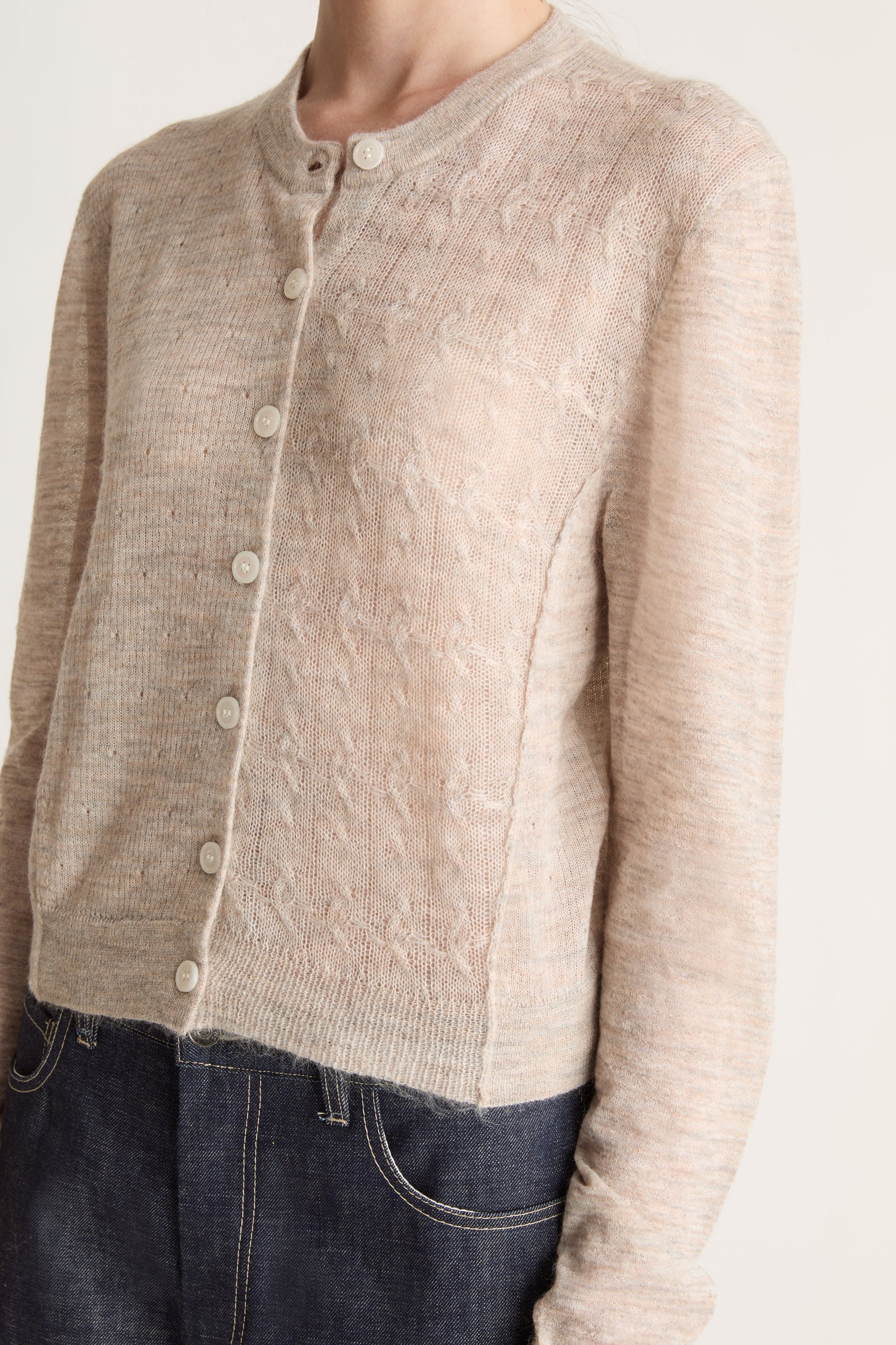 Person wearing a beige cardigan and dark jeans on a white background
