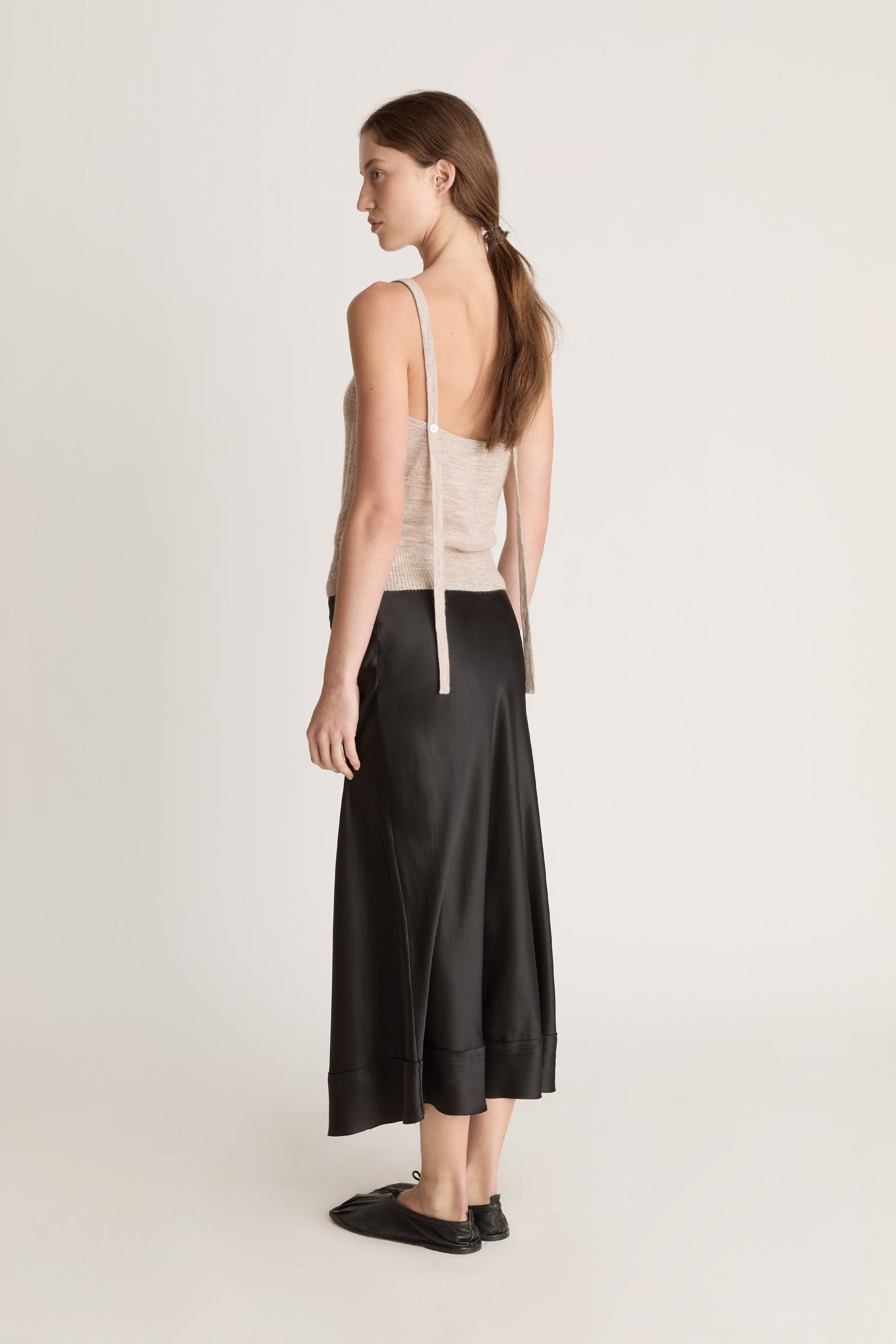 Woman wearing a beige knit cami top and black skirt on a white background