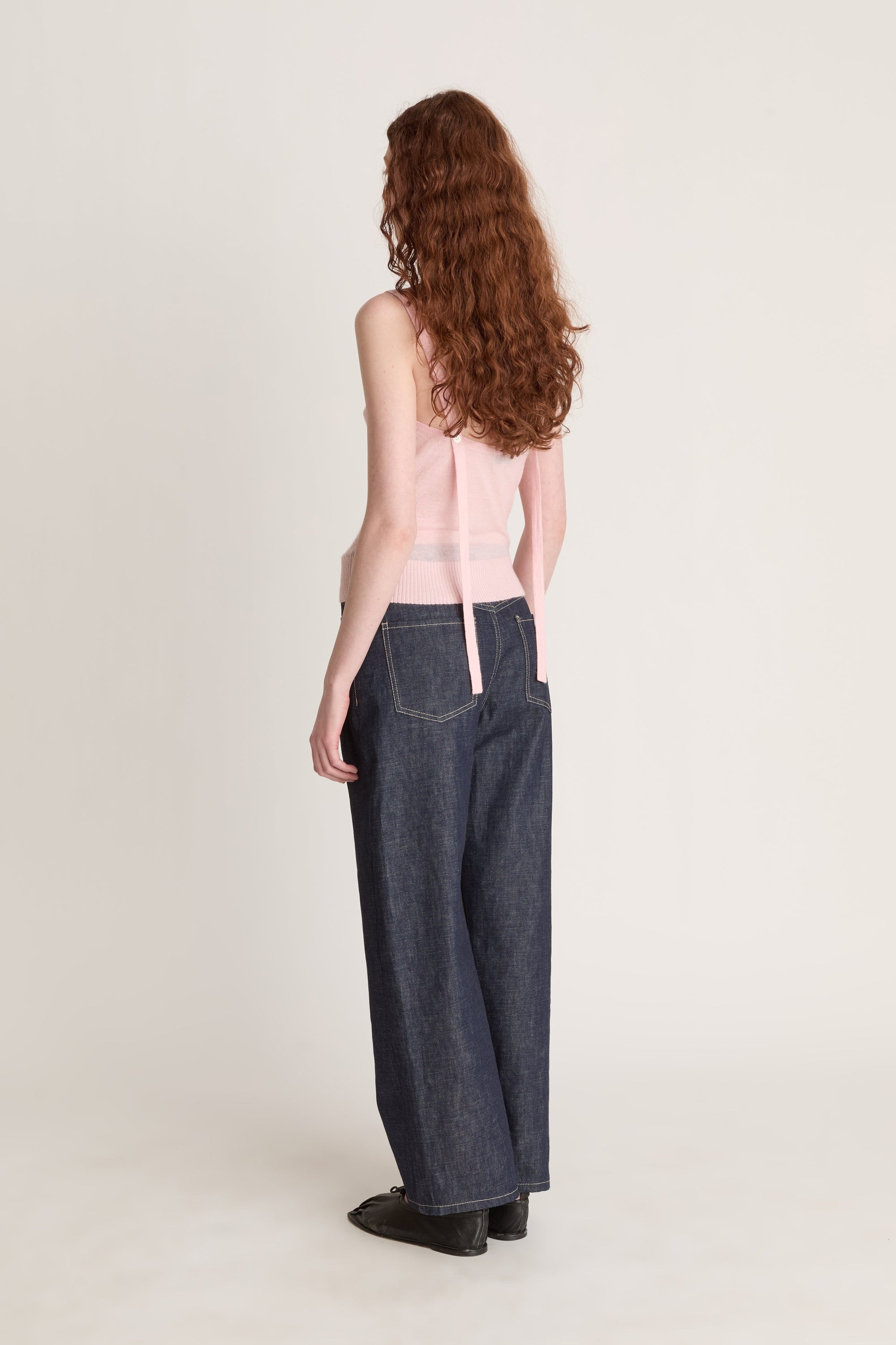 Woman wearing a pink knit top and dark blue jeans on a white background