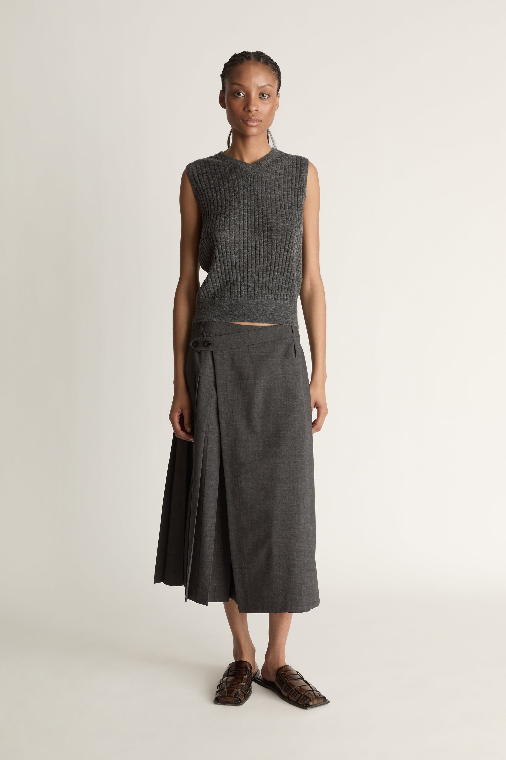 Woman wearing a dark gray sleeveless v neck knit top and skirt on a white background
