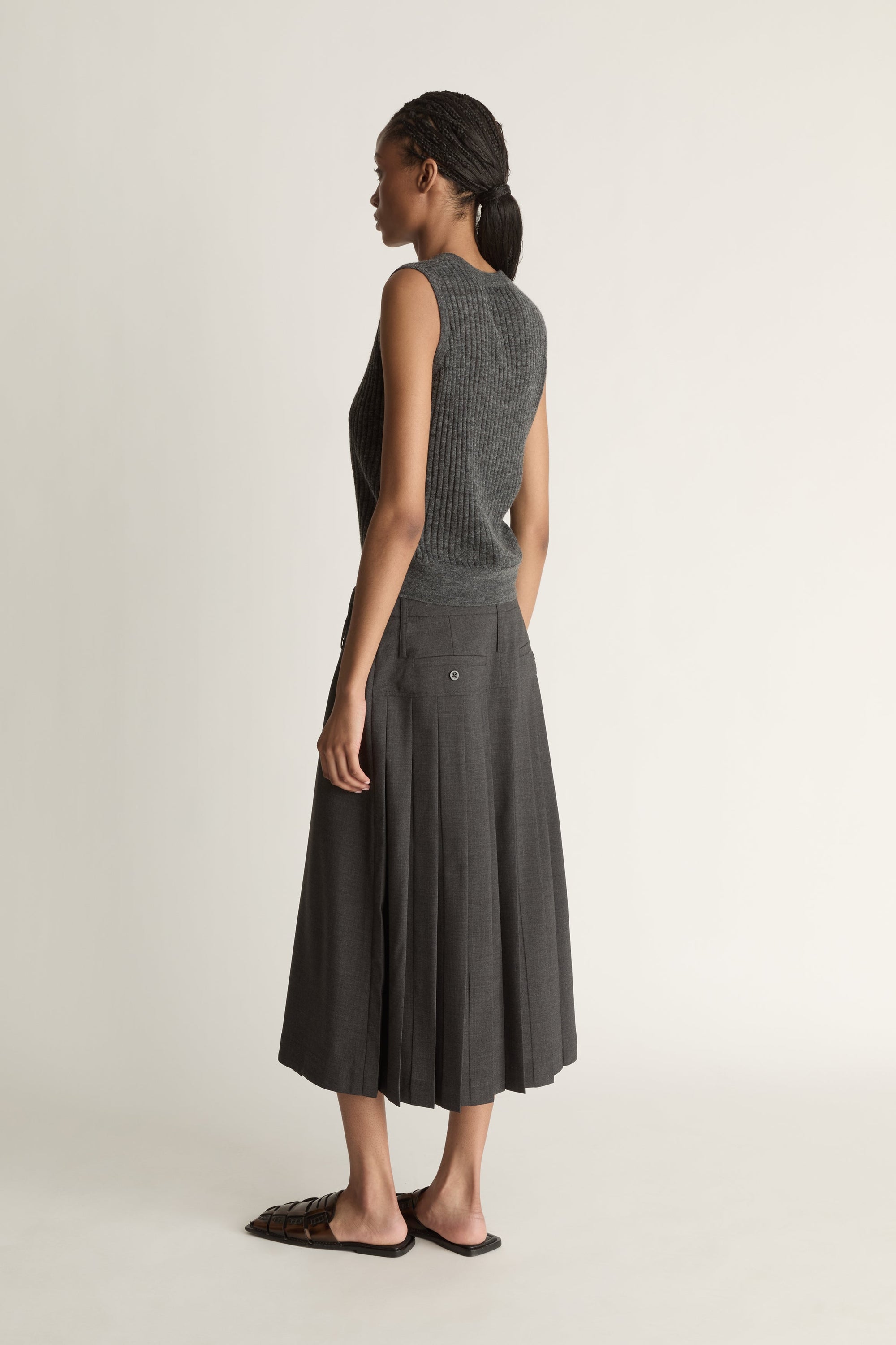 Woman wearing a dark gray sleeveless v neck knit top and skirt on a white background