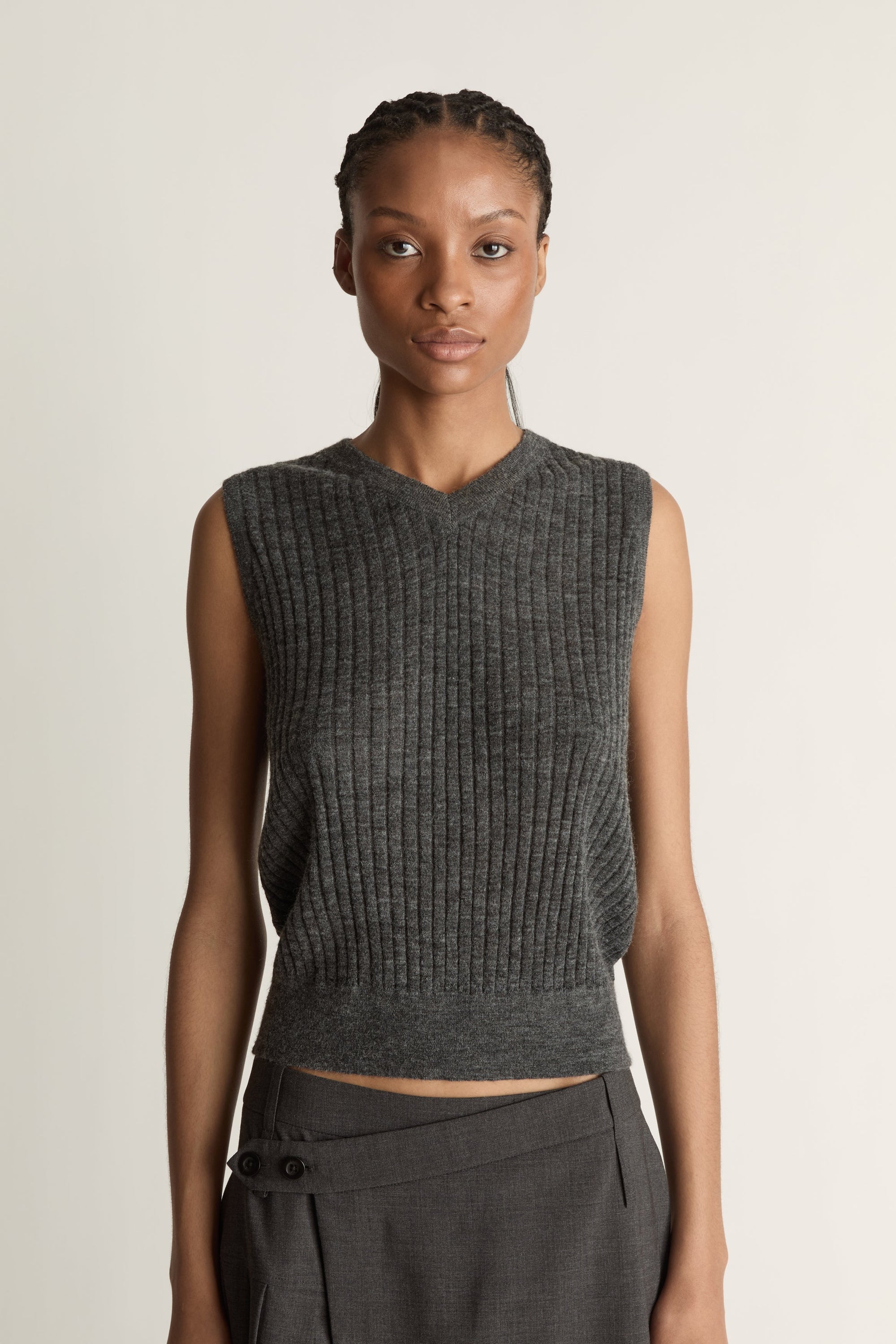 Woman wearing a dark gray sleeveless v neck knit top and skirt on a white background