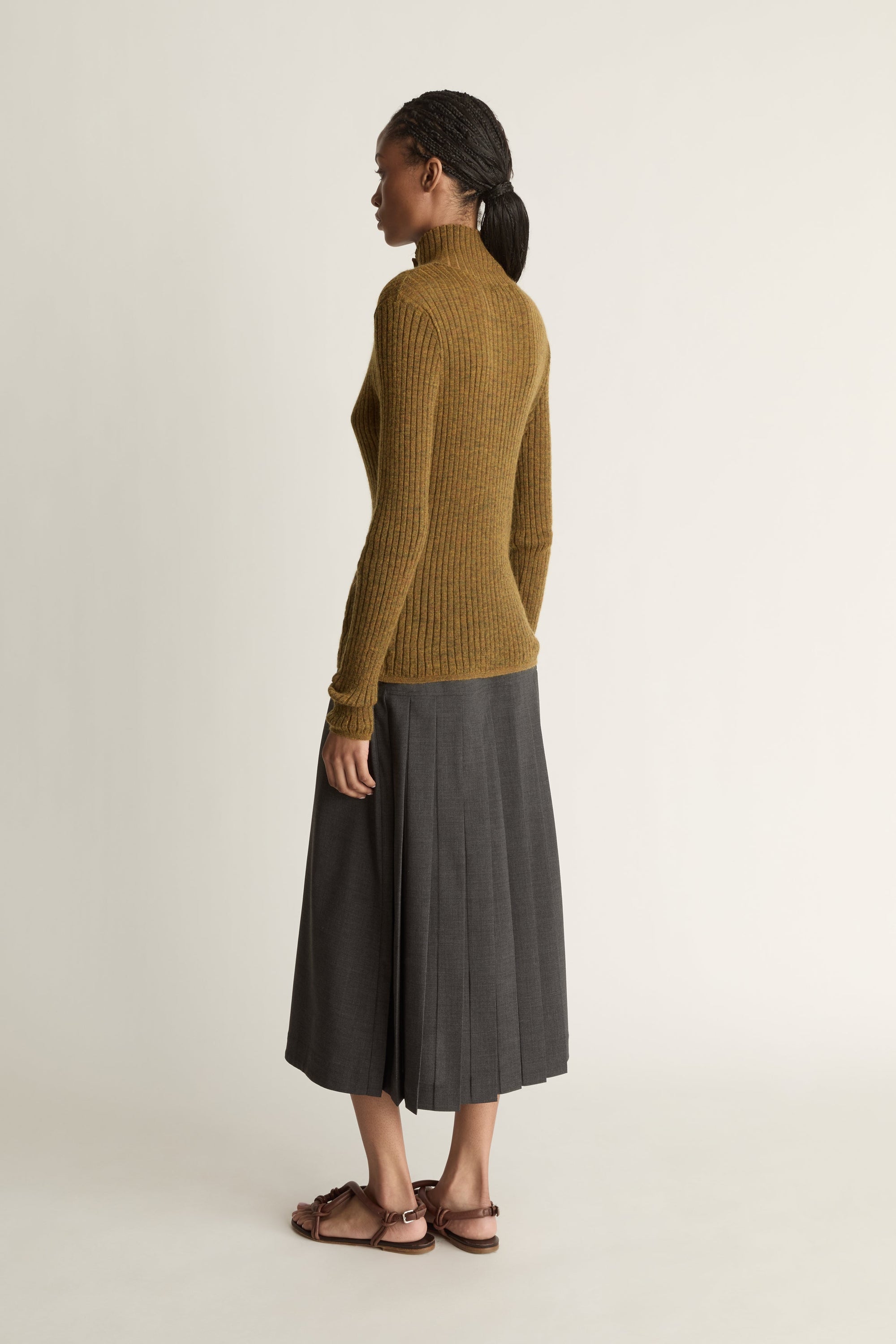 Woman wearing a brown ribbed sweater and gray skirt on a beige background