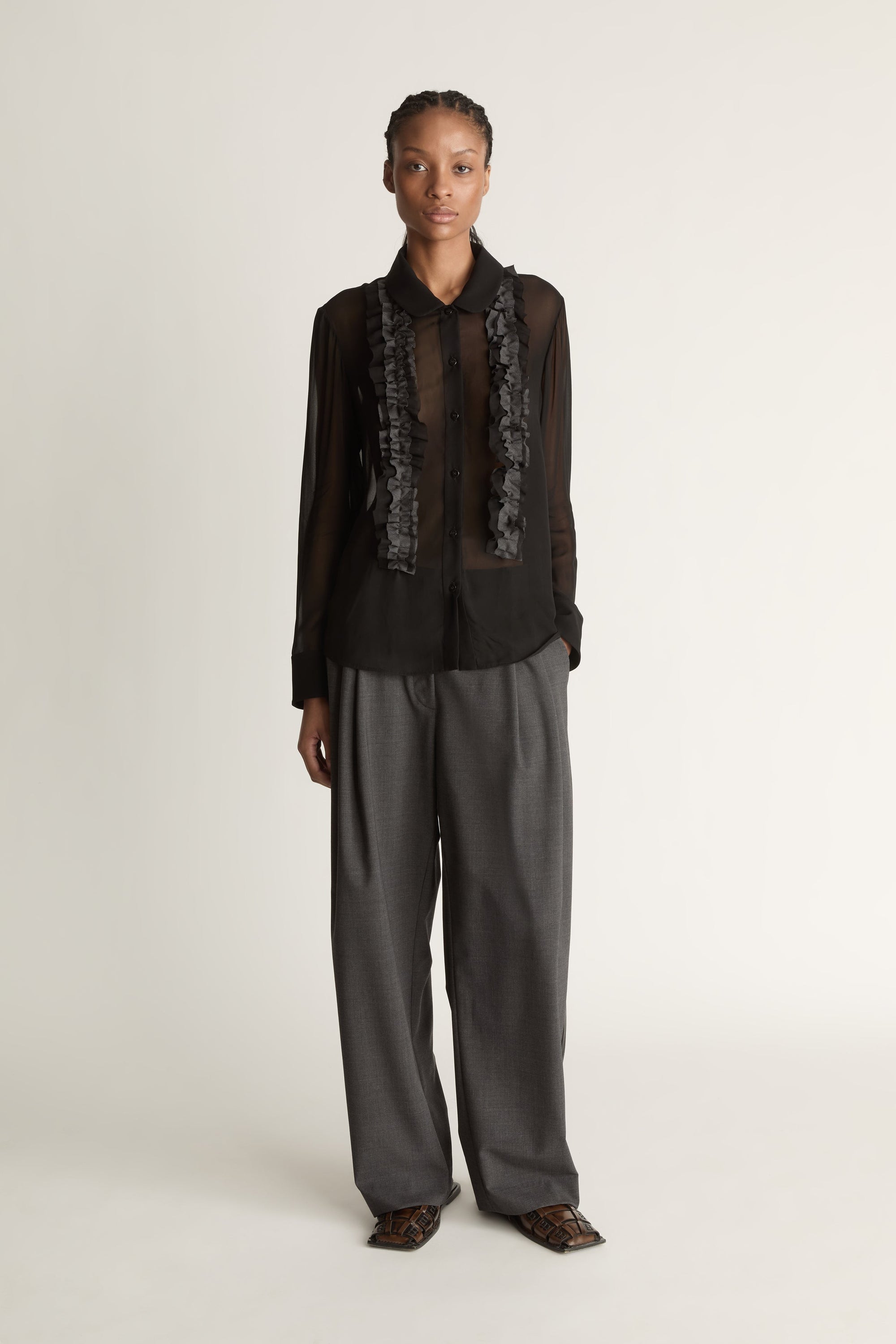 Woman wearing Black sheer shirt and grey trousers on a white background