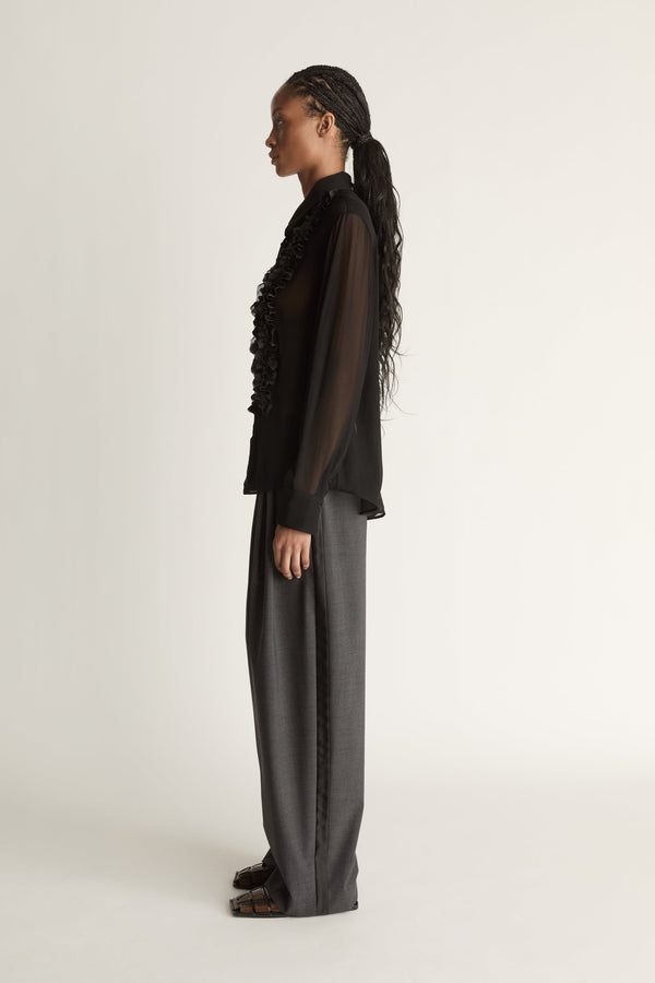 Woman wearing a black sheer shirt and grey trousers on a white background