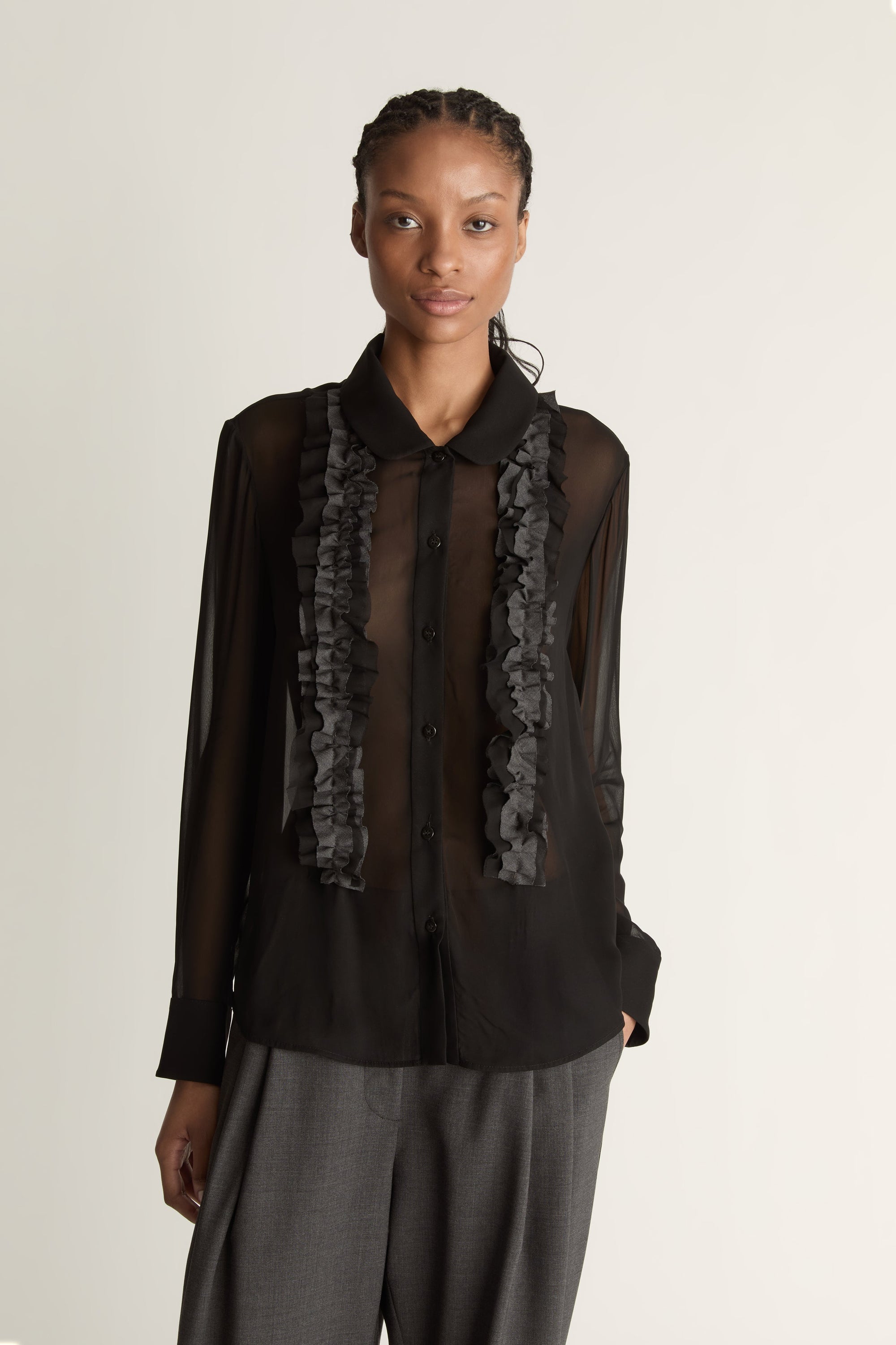 Woman wearing Black sheer shirt and grey trousers on a white background