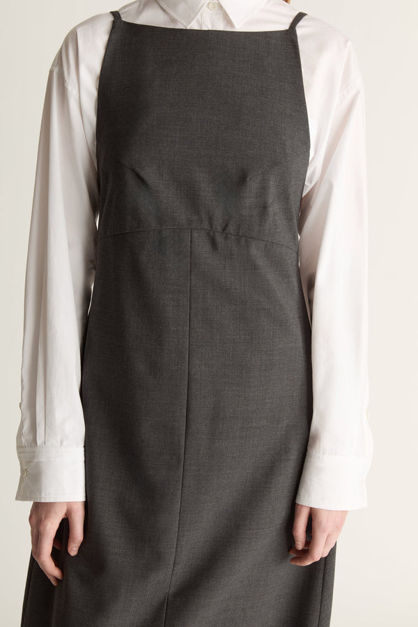 Person wearing a long dark apron style dress over a light shirt on a plain background