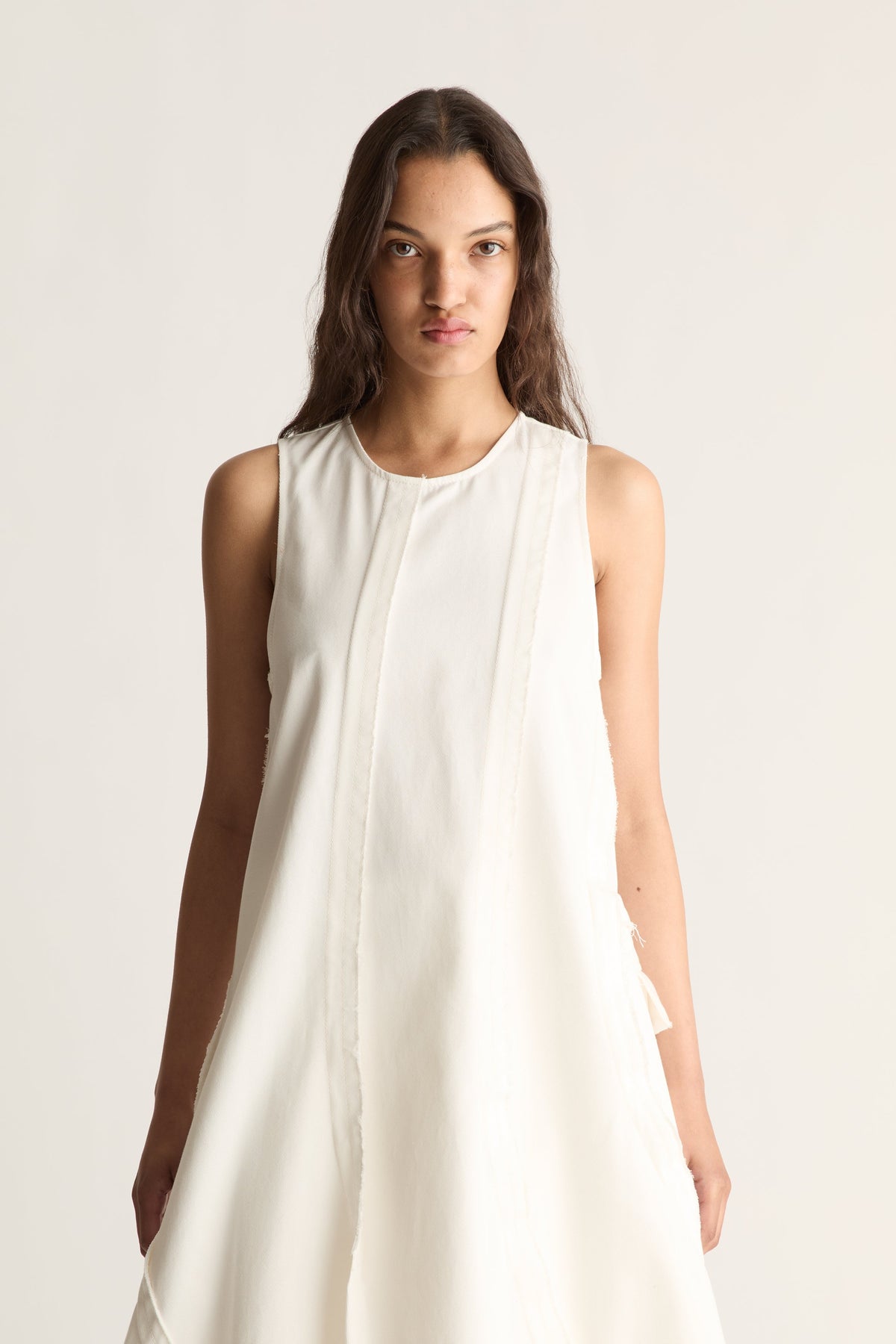 Close-up of a white sleeveless midi dress with round neckline, centre panel seam and curved seams