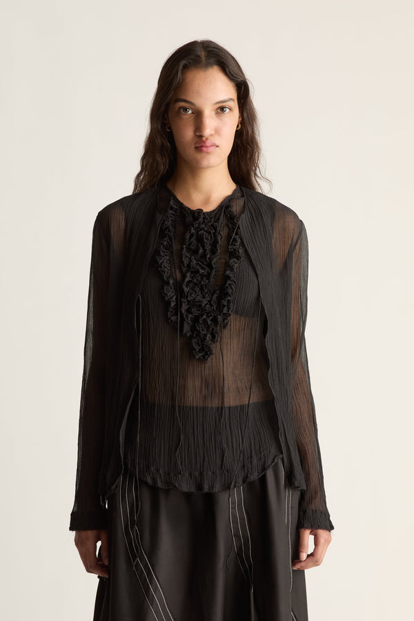 Close-up of a sheer pleated black cardigan layered over a black ruffle bib top