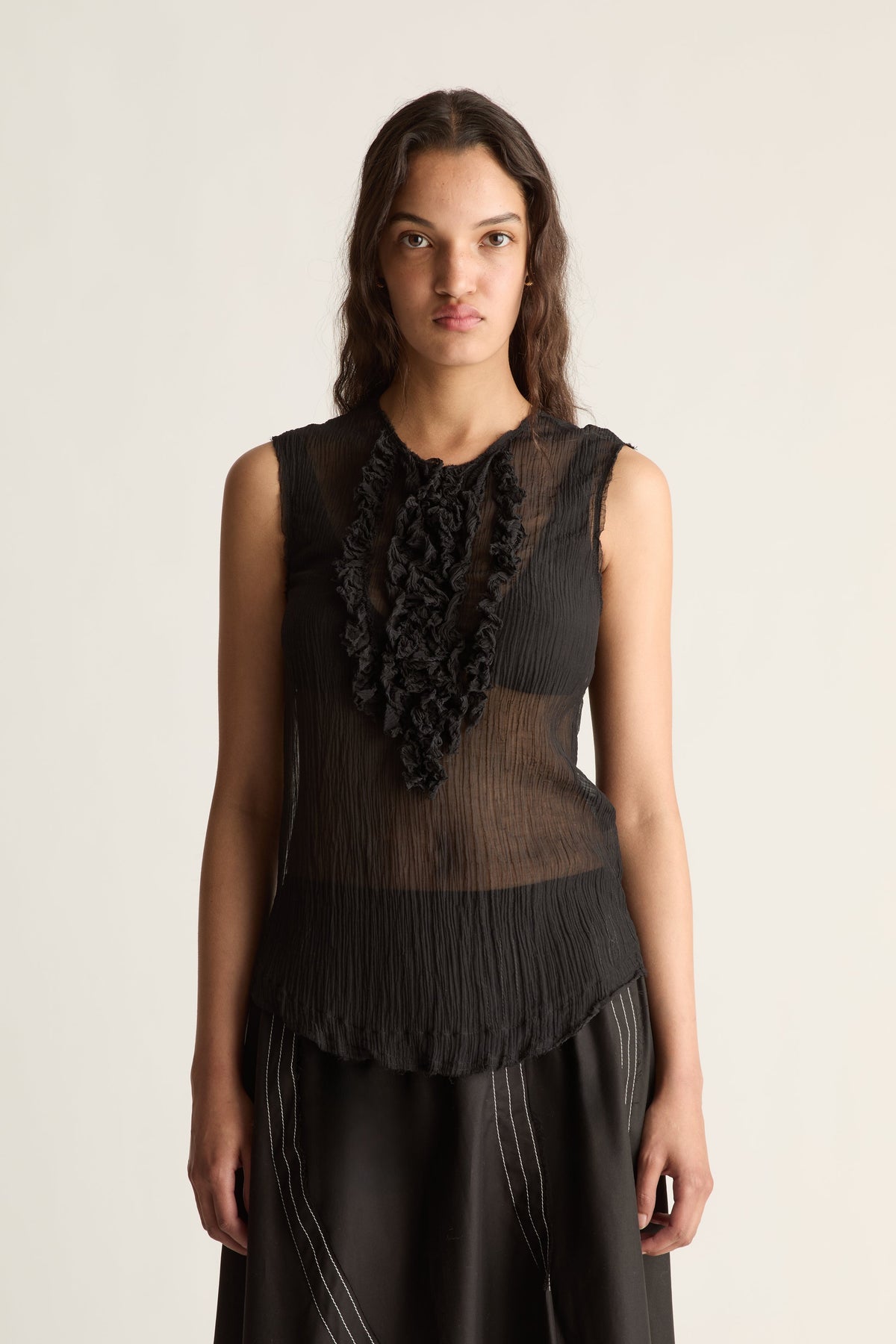 Close-up of a sheer pleated black top with ruffle bib and scalloped hem