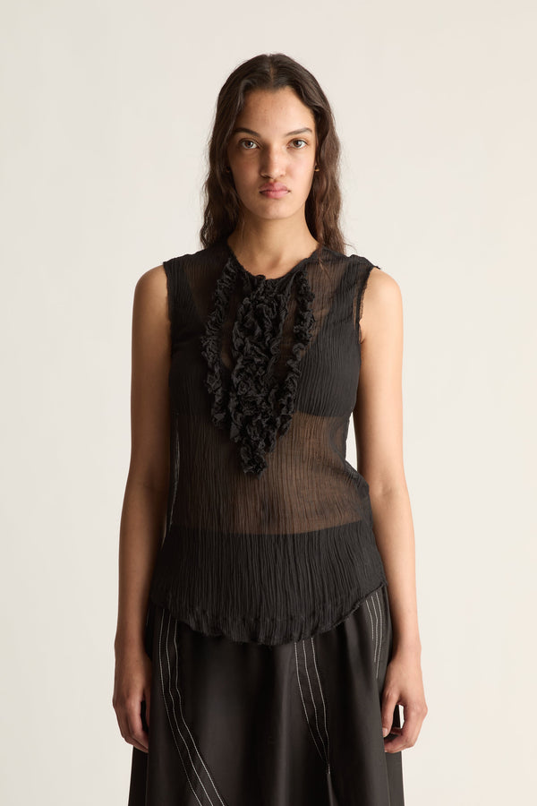 Close-up of a sheer pleated black top with ruffle bib and scalloped hem