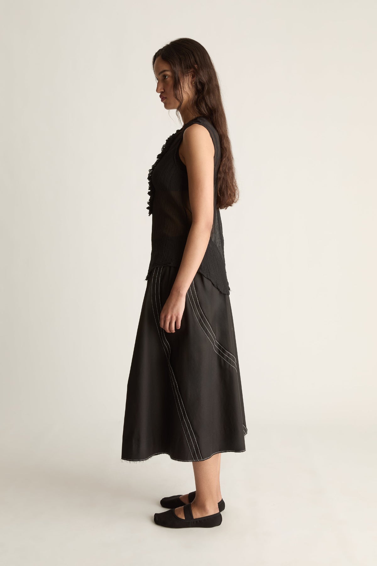 Side view of a woman in a sheer black sleeveless top and flared black skirt with diagonal stitching