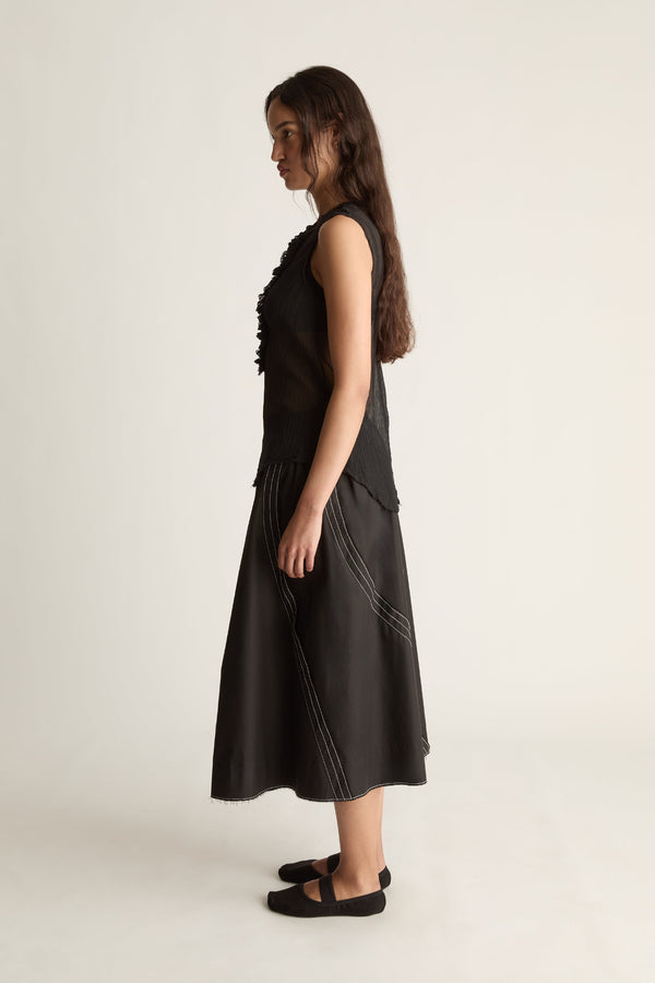 Side view of a woman in a sheer black sleeveless top and flared black skirt with diagonal stitching
