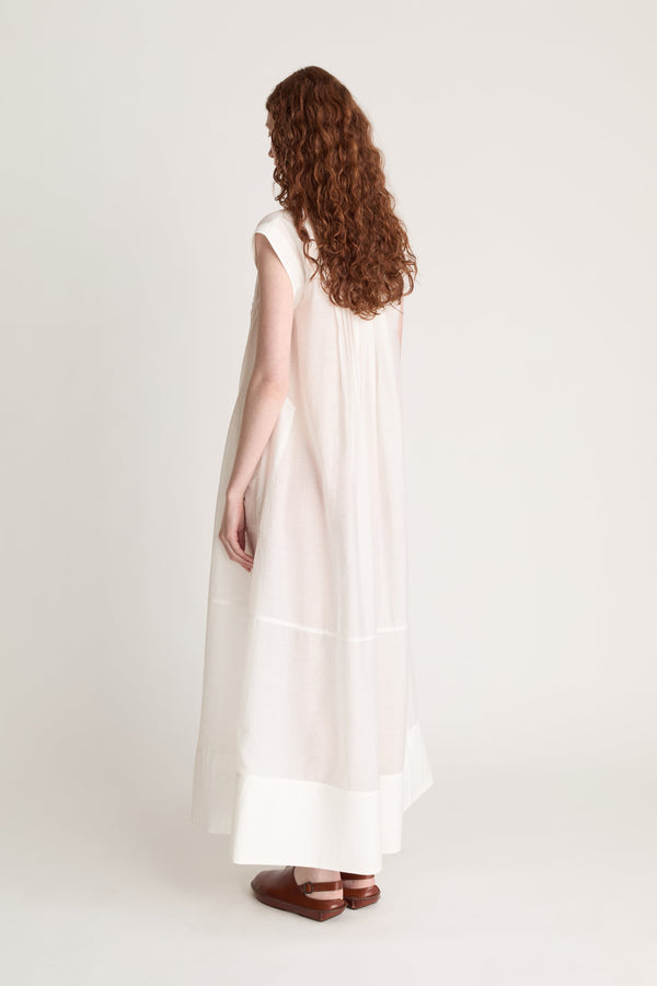 Woman wearing a long white dress with brown shoes on a white background
