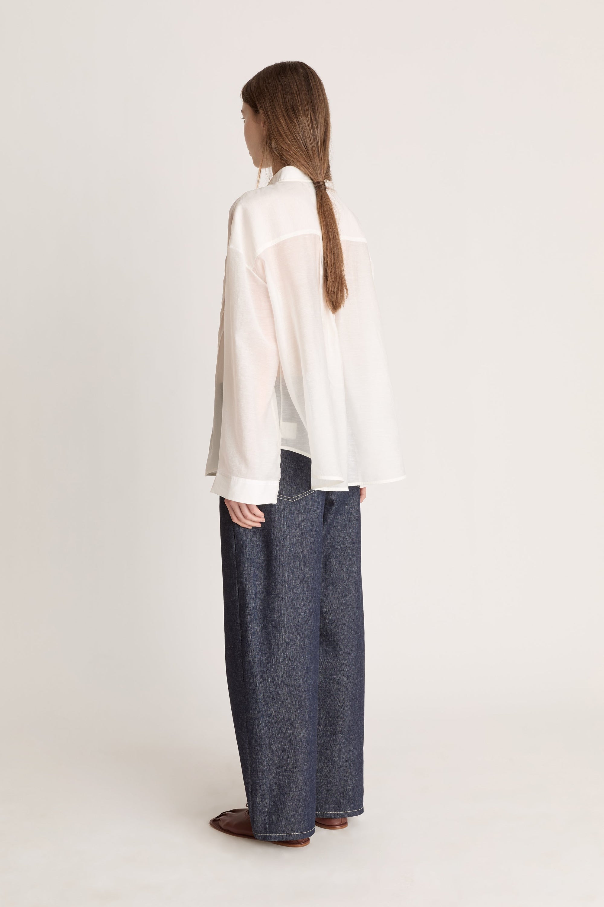 Person wearing a light-colored blouse and dark pants on a white background