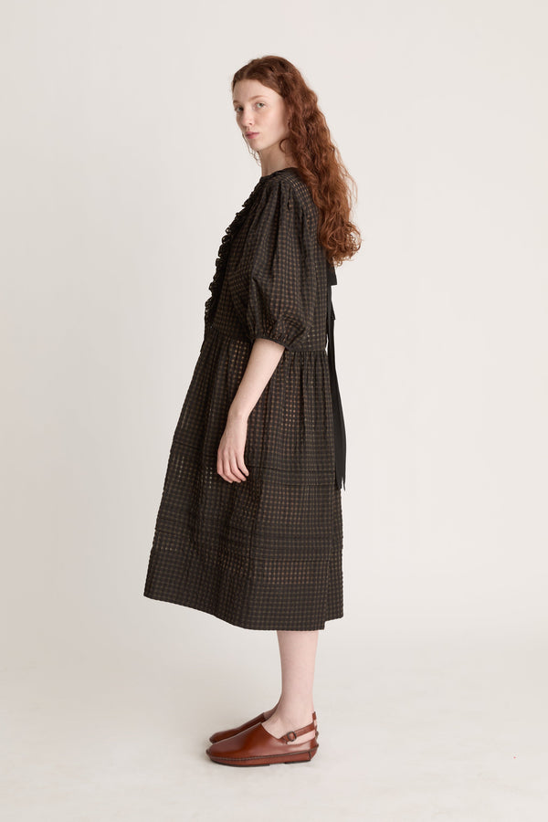 Woman wearing a dark checkered dress  with puffy sleeves with ruffled details on a white background