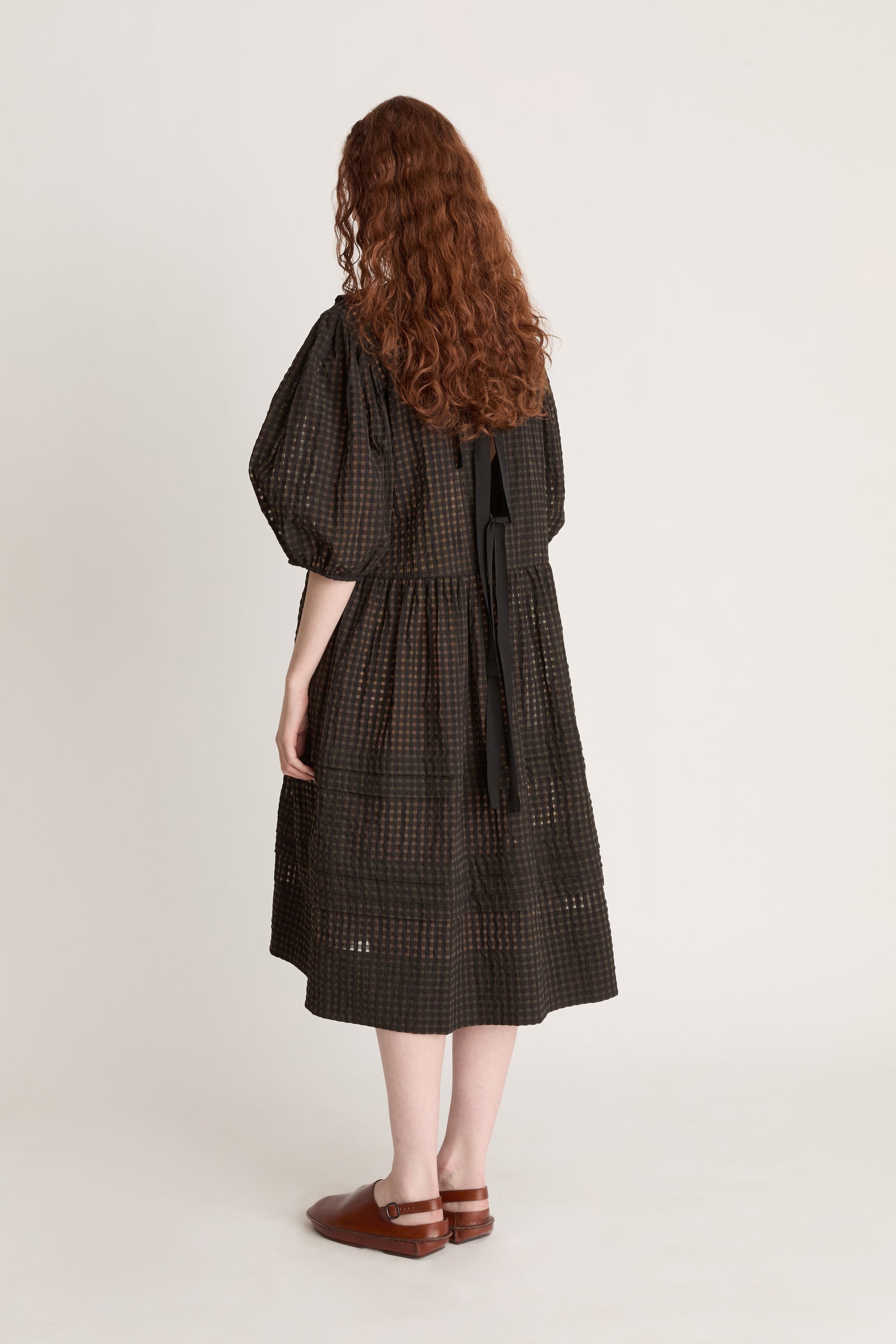 Woman wearing a dark checkered dress  with puffy sleeves with ruffled details on a white background