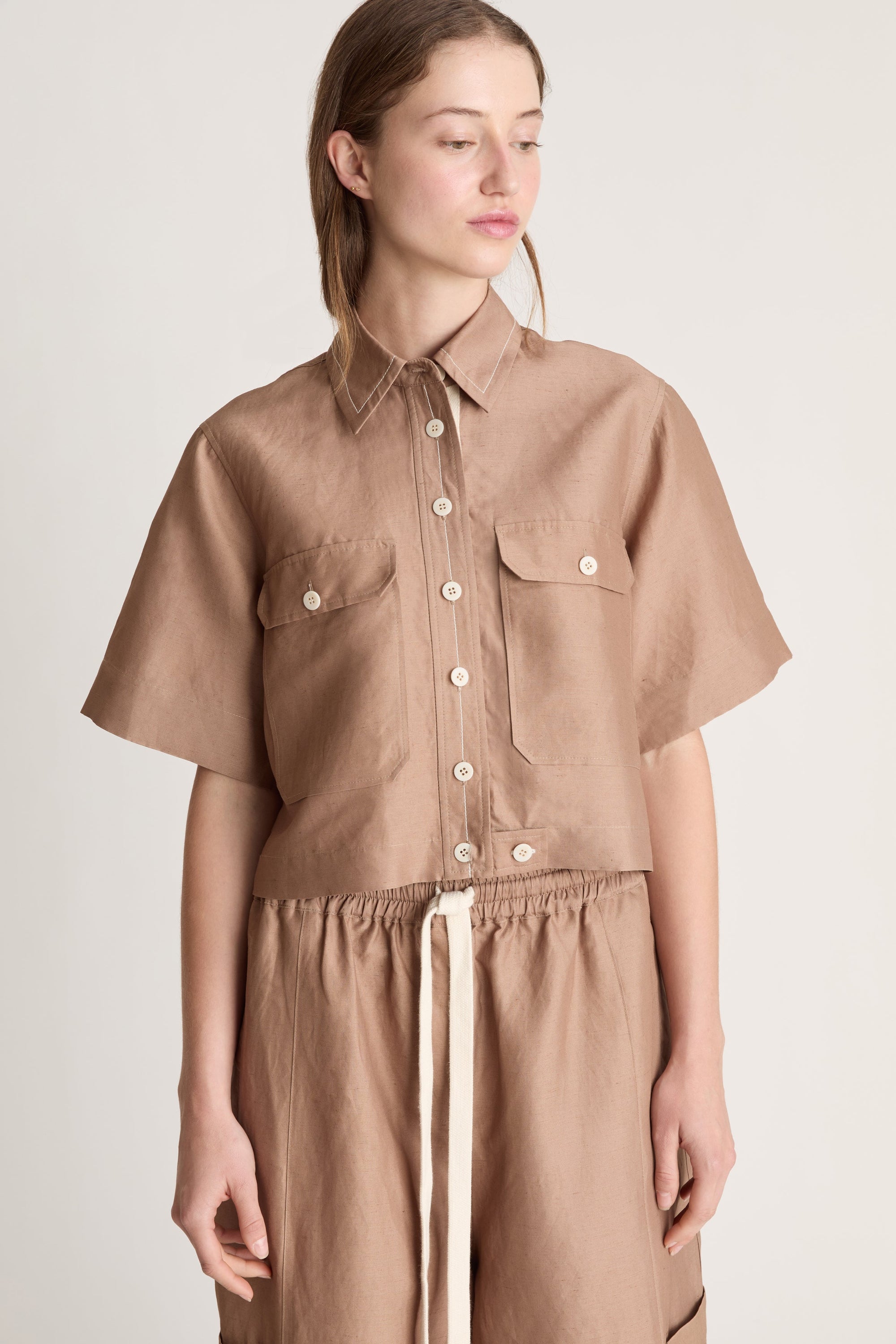Woman wearing a brown button up short sleeve shirt and brown pants on a white background 