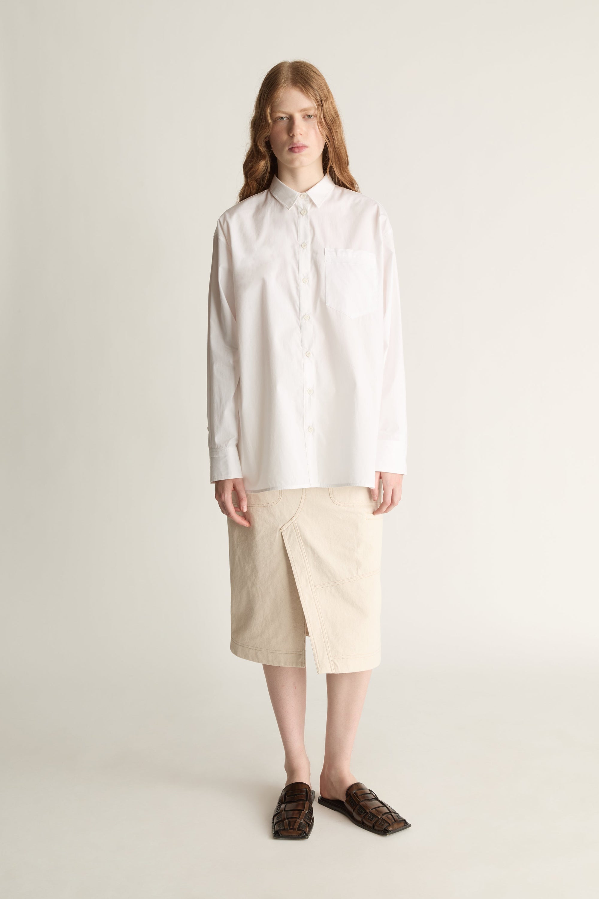 Person wearing a white shirt and beige skirt on a plain background