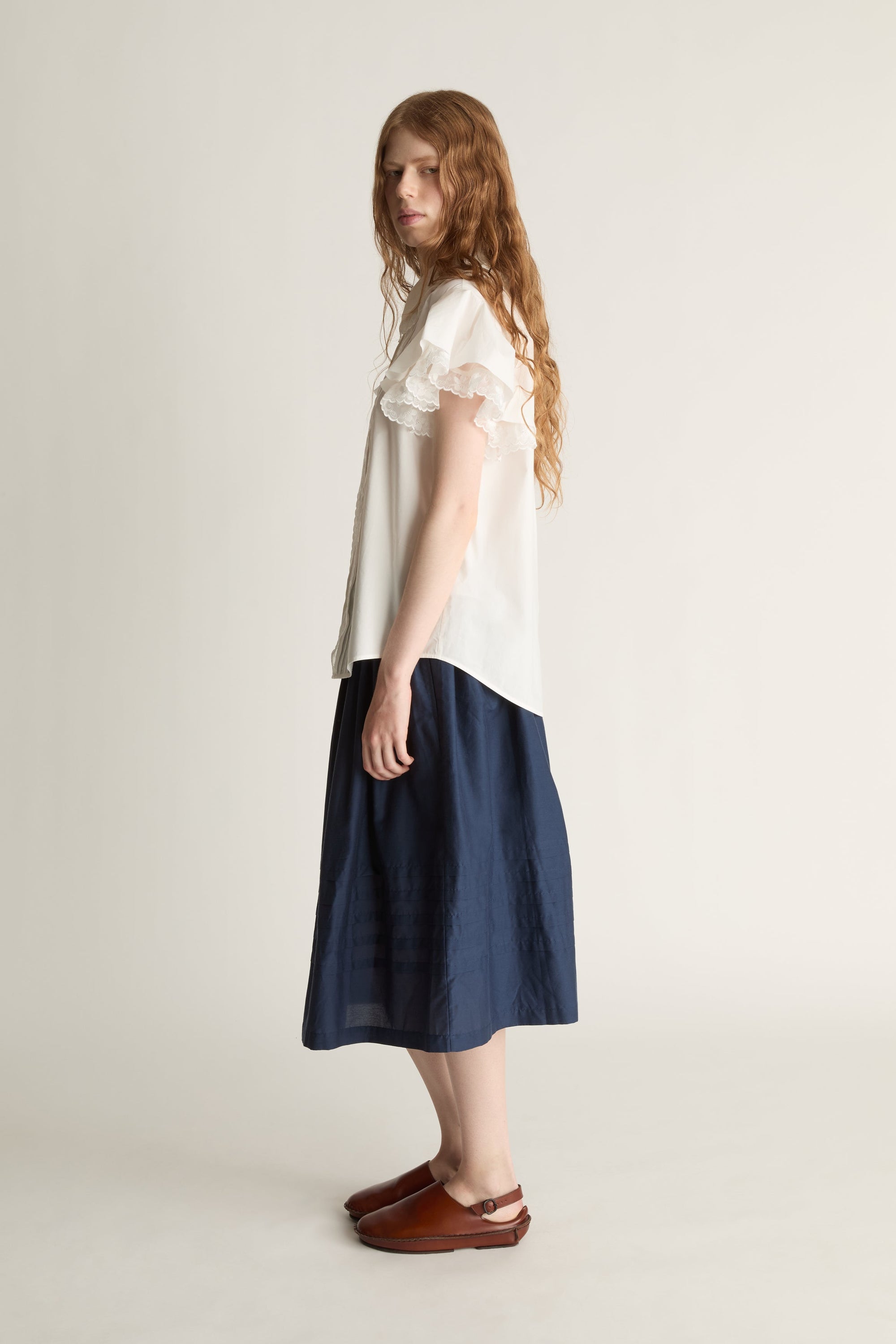 Woman wearing a white blouse and navy skirt on a plain background