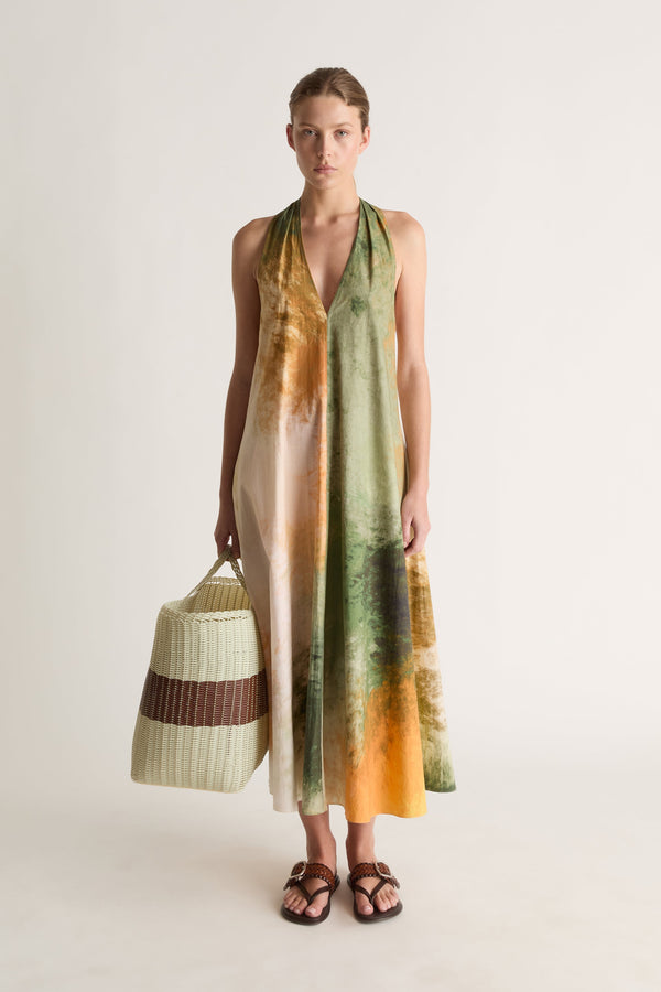 Front view of a woman in a green and orange print halter dress holding a cream woven basket with brown stripe