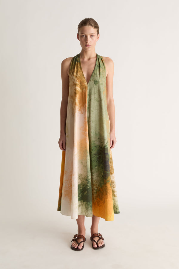 Front view of a woman wearing a green and orange watercolour-print halter midi dress with brown sandals against a white studio background