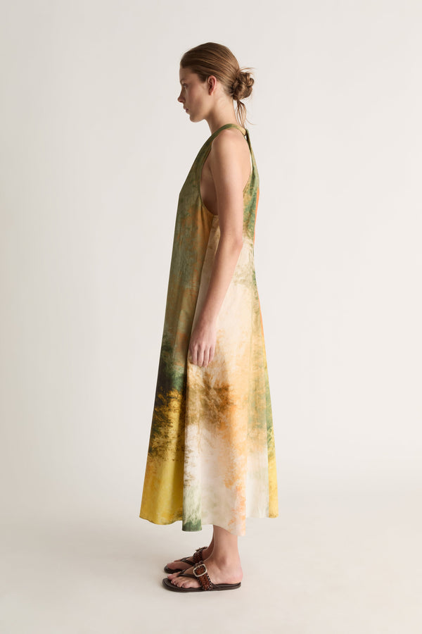 Side profile of a woman with a bun in a halter-neck dress with a green, yellow and orange print