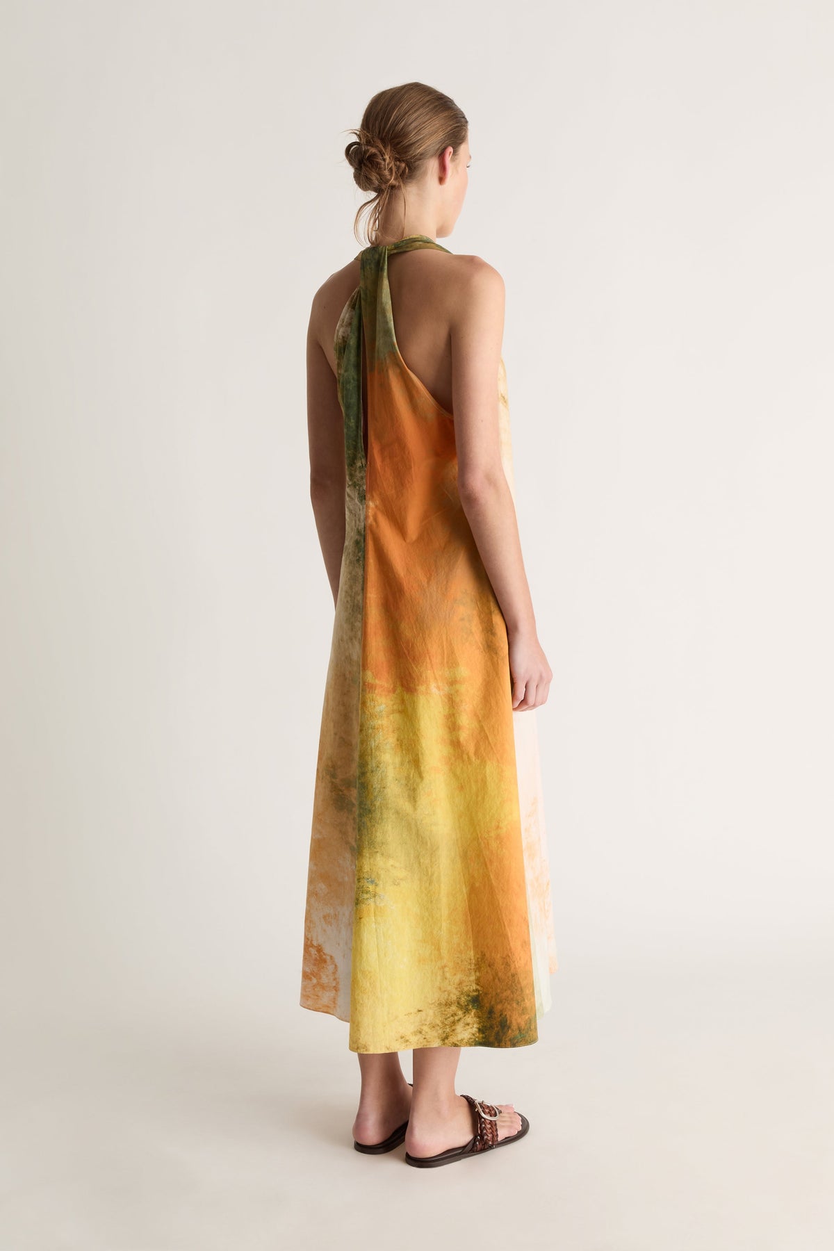 Back view of a woman in a racer-back halter dress with an orange and yellow watercolour print