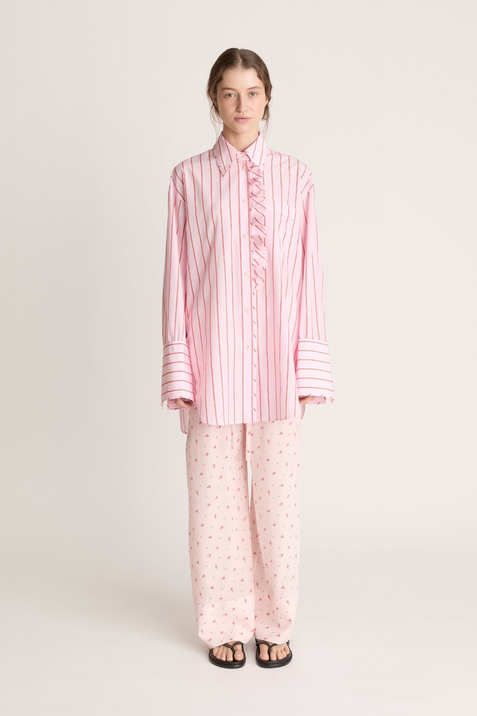 Woman wearing a pink striped shirt and pink floral pant on a white background