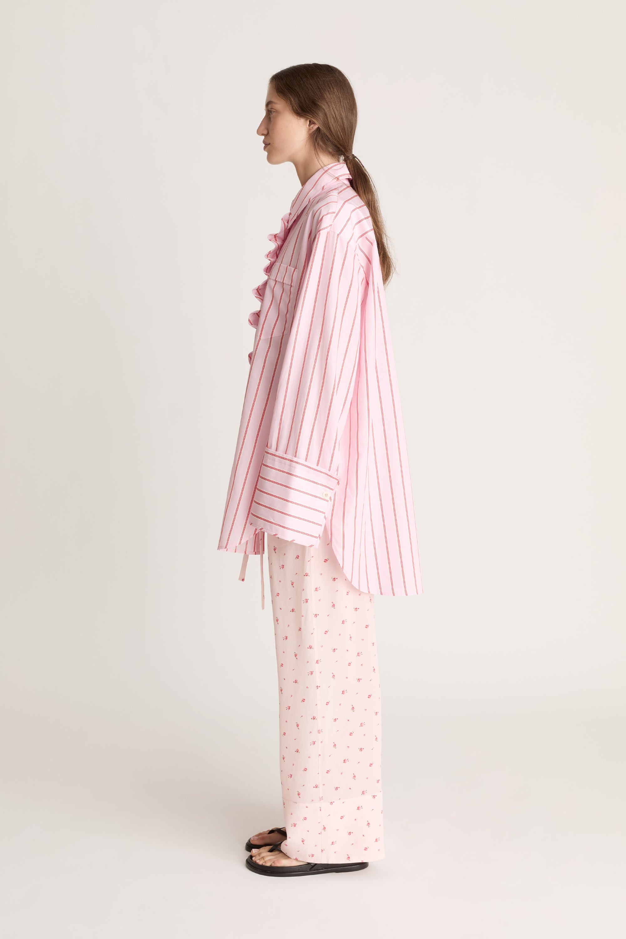 Woman wearing a pink striped shirt with floral pink pants on a white background