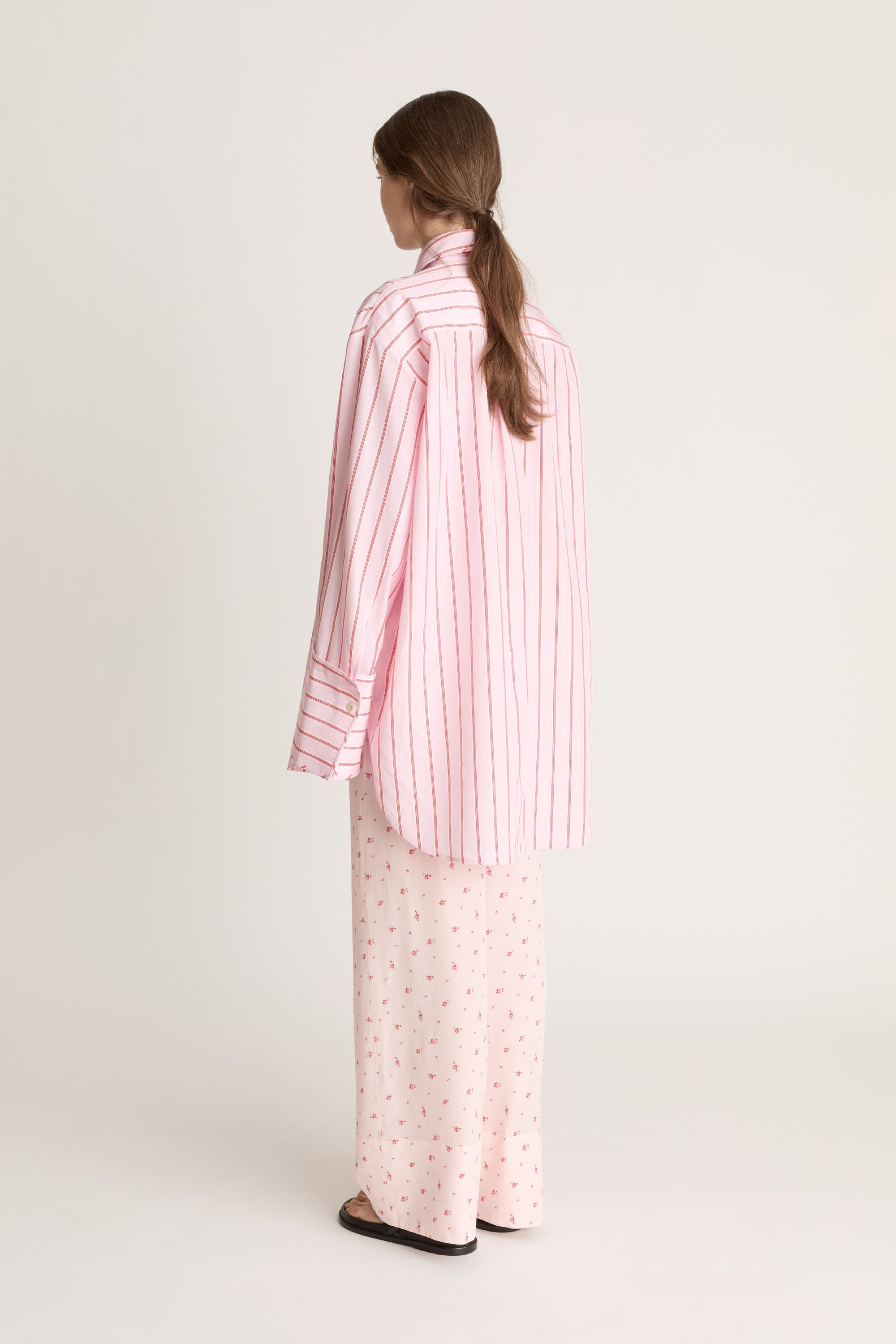Woman wearing a pink striped shirt and pink floral pants on a white background