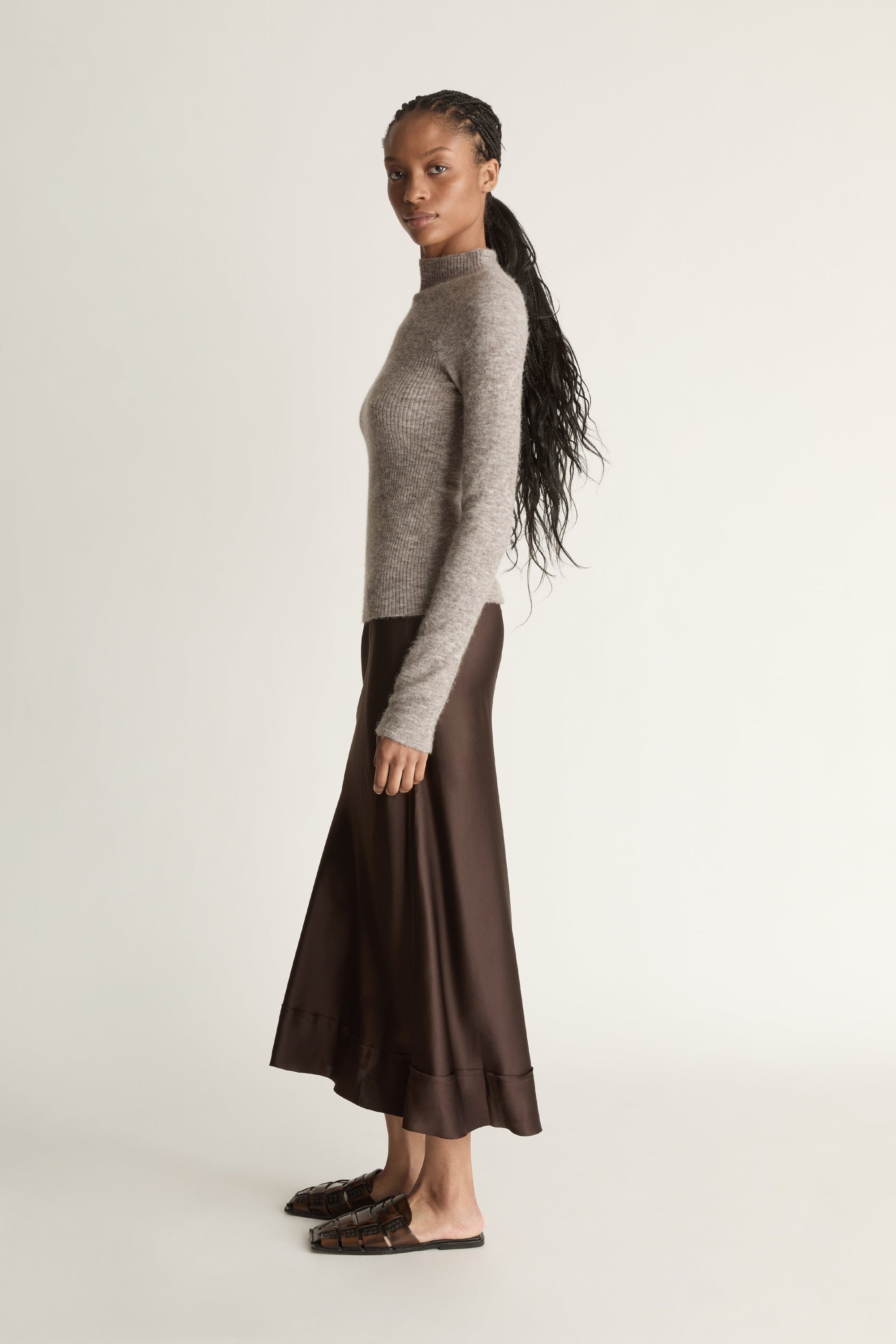 Woman wearing a gray turtleneck sweater and brown skirt against a beige background