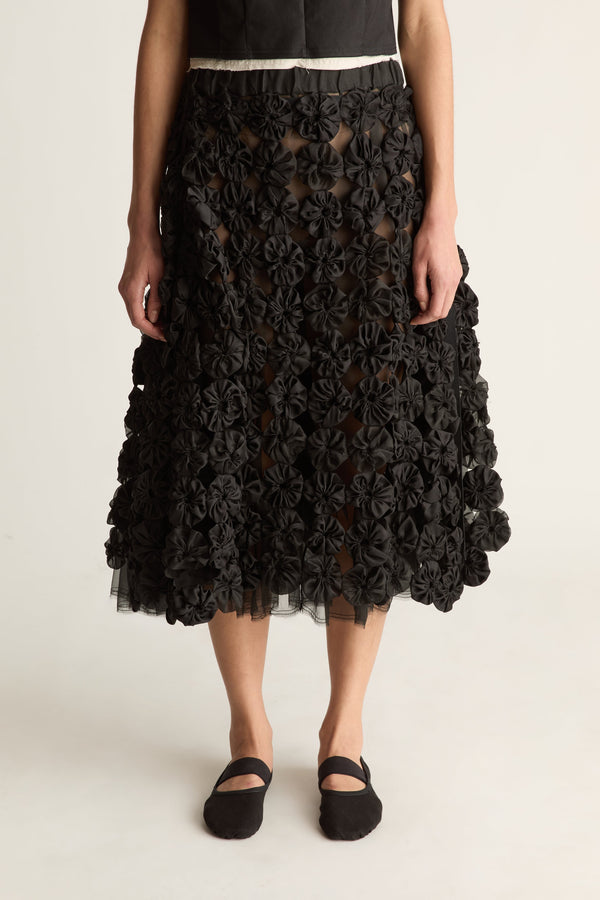 Close-up of a black fabric rosette skirt with sheer cut-outs and tulle hem, worn with a black top