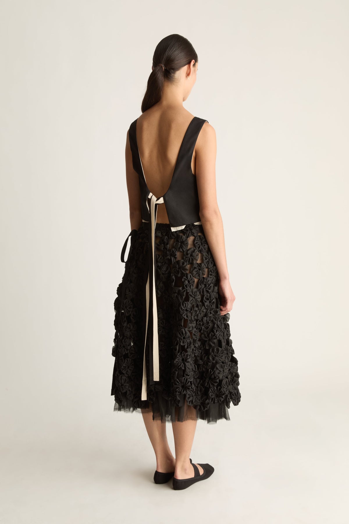 Back view of a woman in a black open-back top with ribbon ties and a black rosette skirt over a tulle underlayer